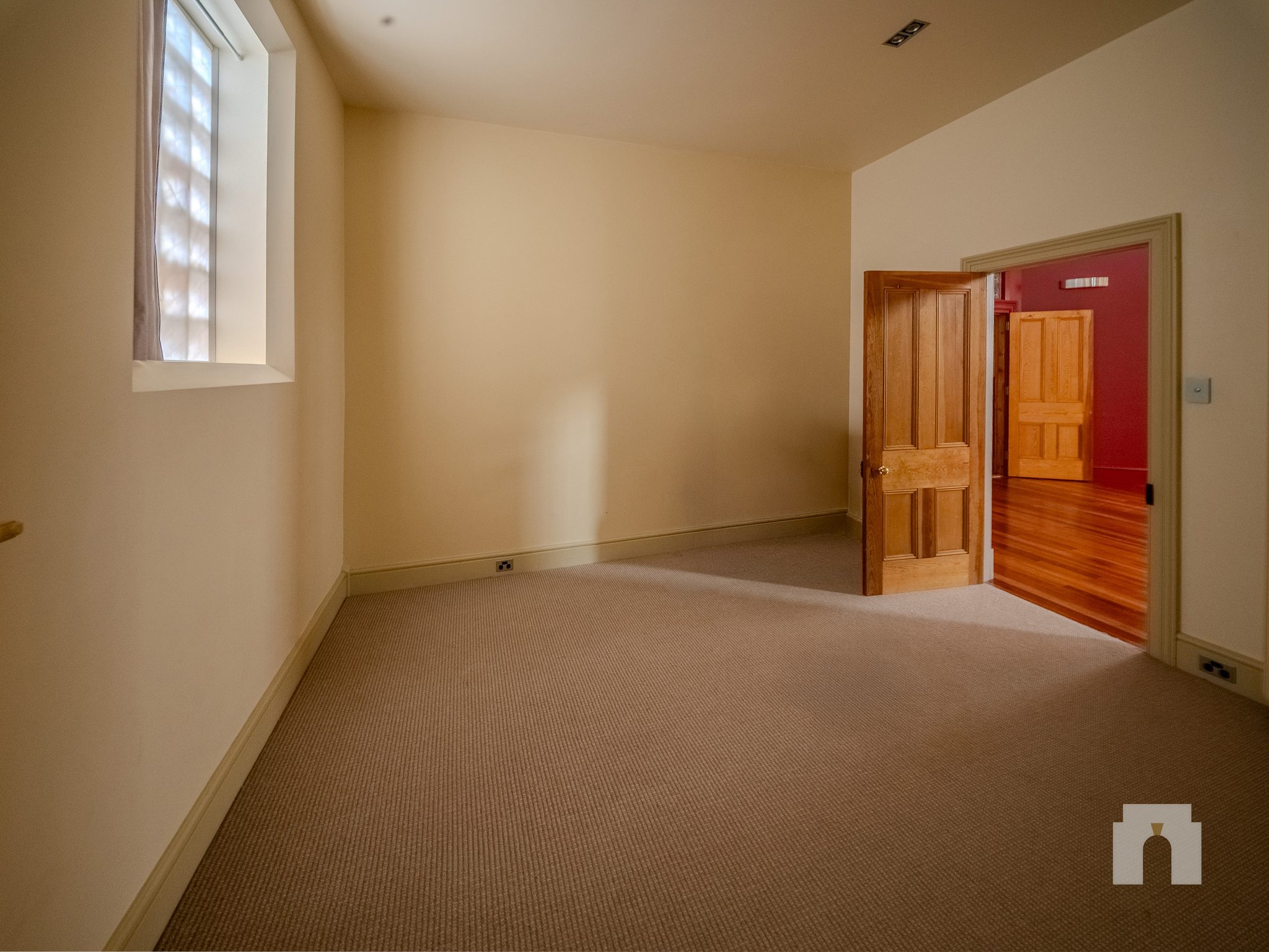 Empty carpeted room with a glass block window, door open to a red walled corridor beyond.