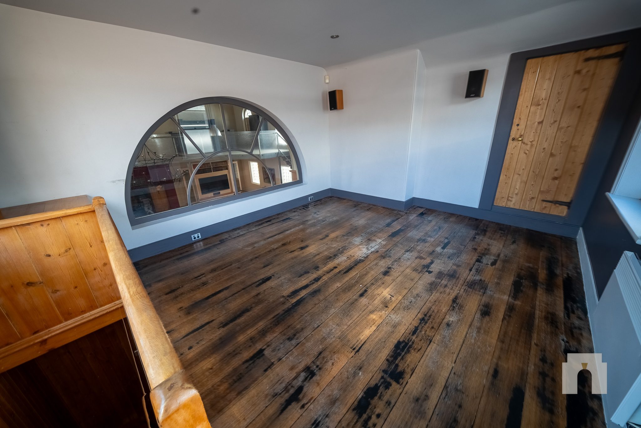 Upper room with worn floorboards and an arched internal window looking over the hall below.
