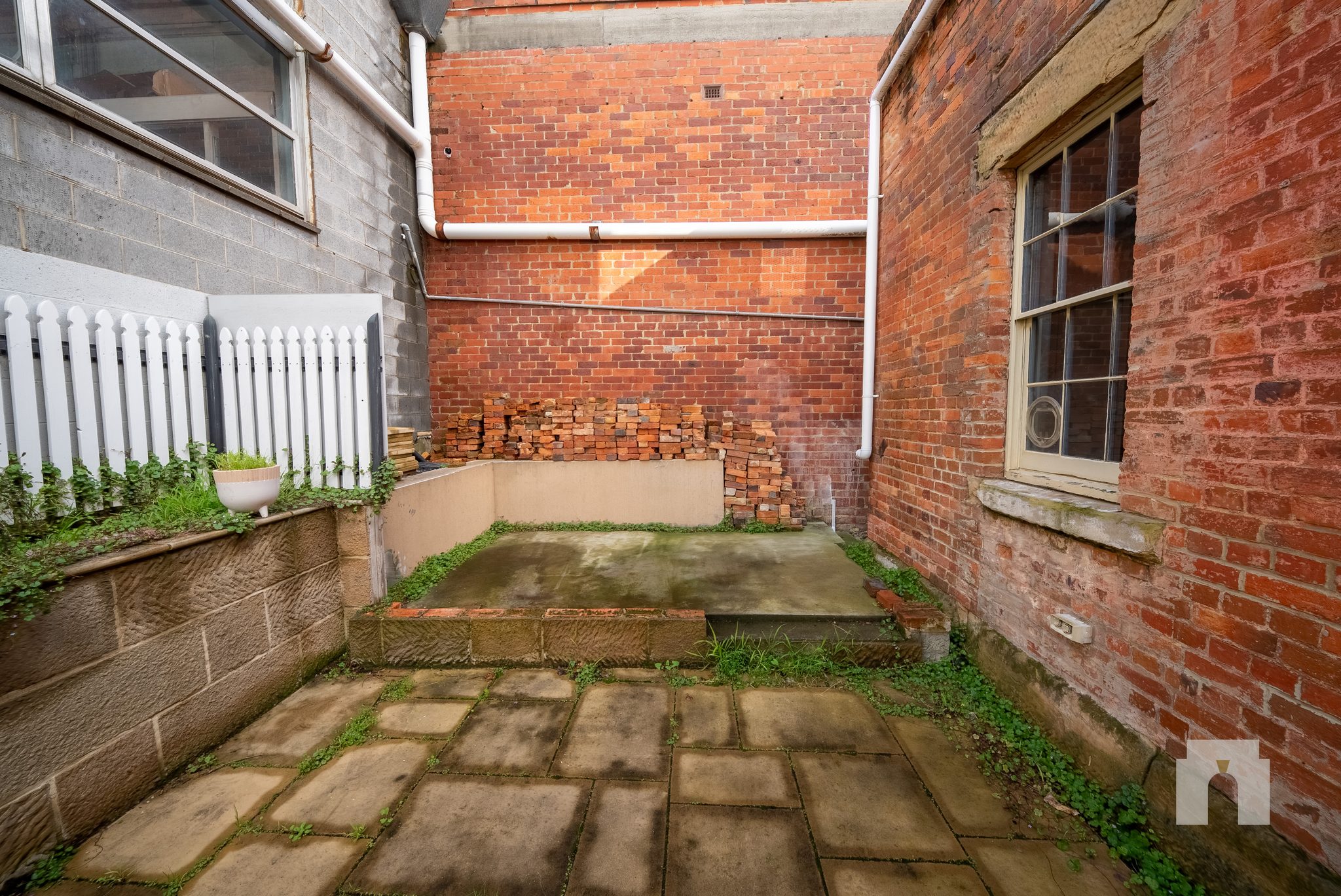 Enclosed paved courtyard between brick walls, with stacked bricks along the rear wall.