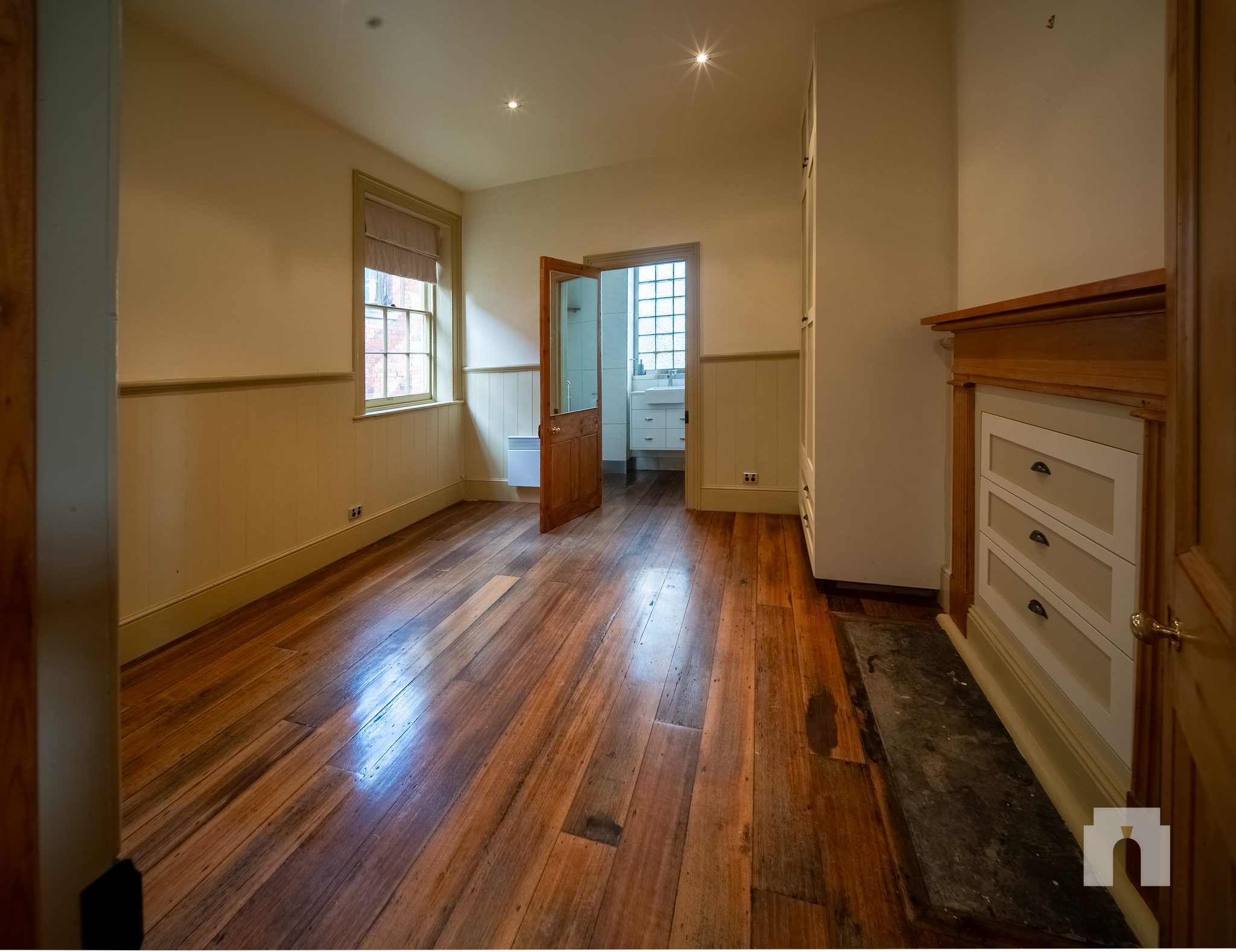 Room with timber floorboards, timber mantel and built-in drawers, door open to a bathroom.
