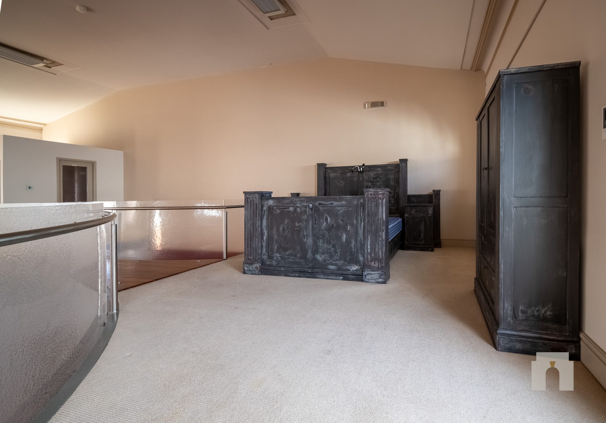 Carpeted mezzanine behind a curved glass balustrade, with a dark timber bed and wardrobe.