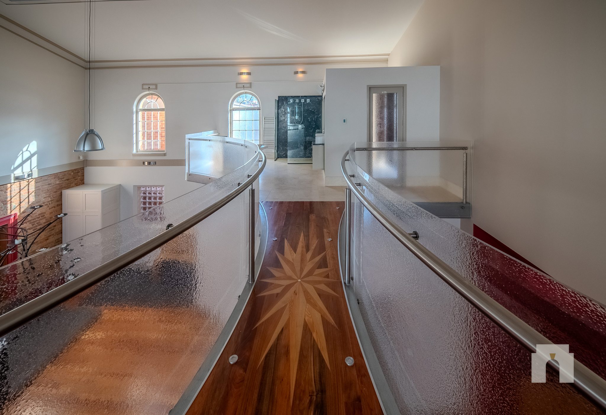 Mezzanine walkway between glass balustrades, star motif inlaid in the timber floor.