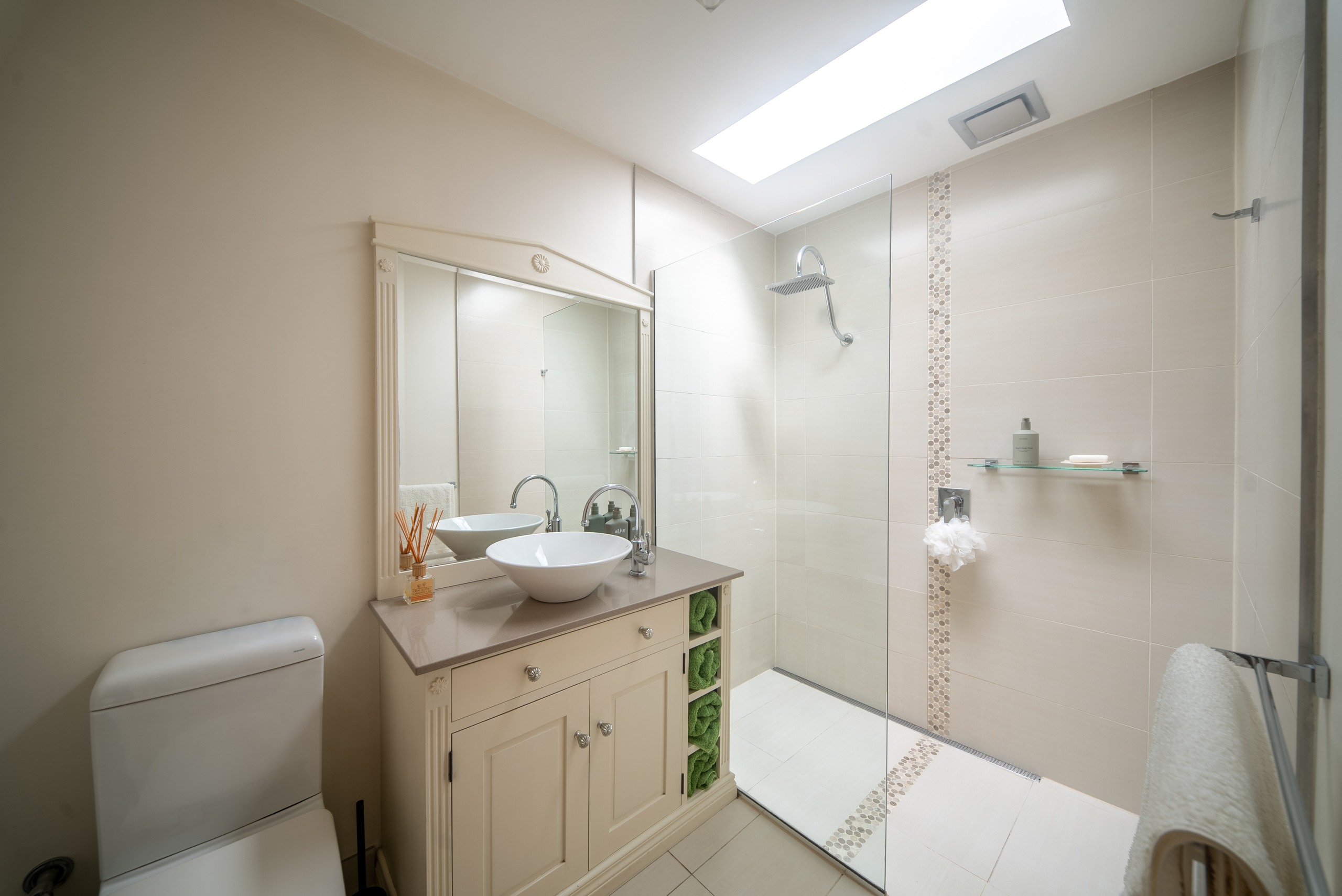 A bathroom with a vessel basin on a cream vanity, a walk-in shower with a feature tile strip, and a skylight.