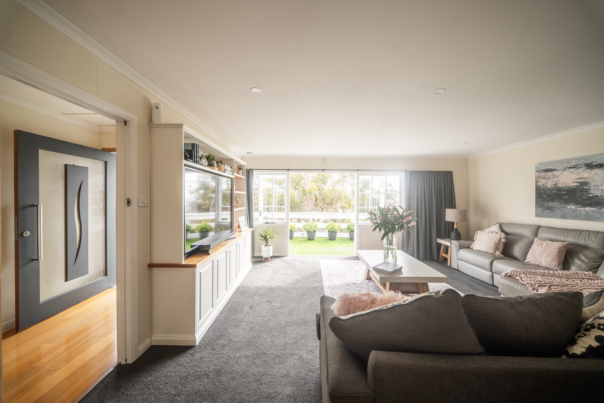 A second living room with a dark sofa and a built-in entertainment unit, opening to the garden through glass doors.
