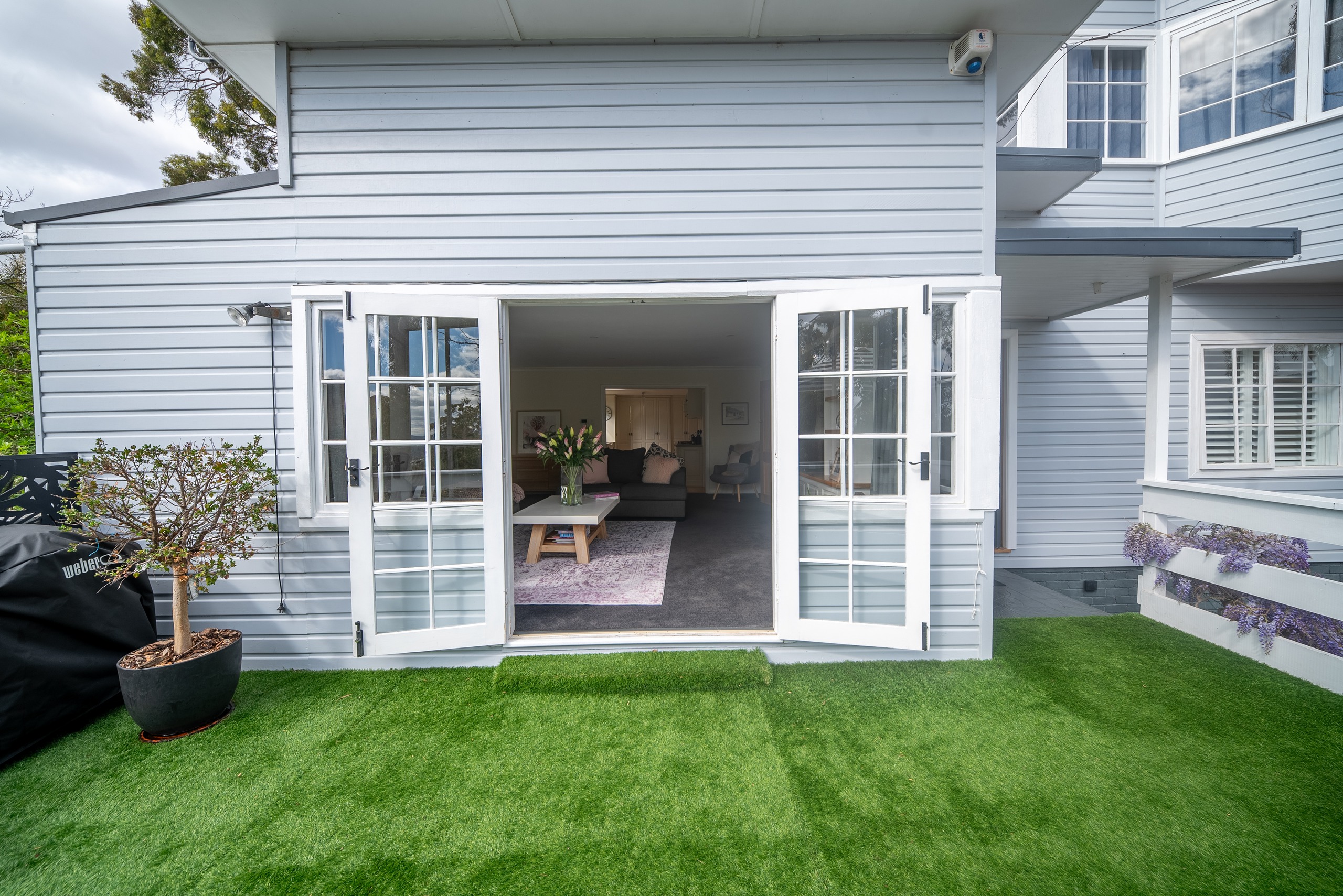 French doors open from the living room onto a level lawn beside the grey weatherboard house.