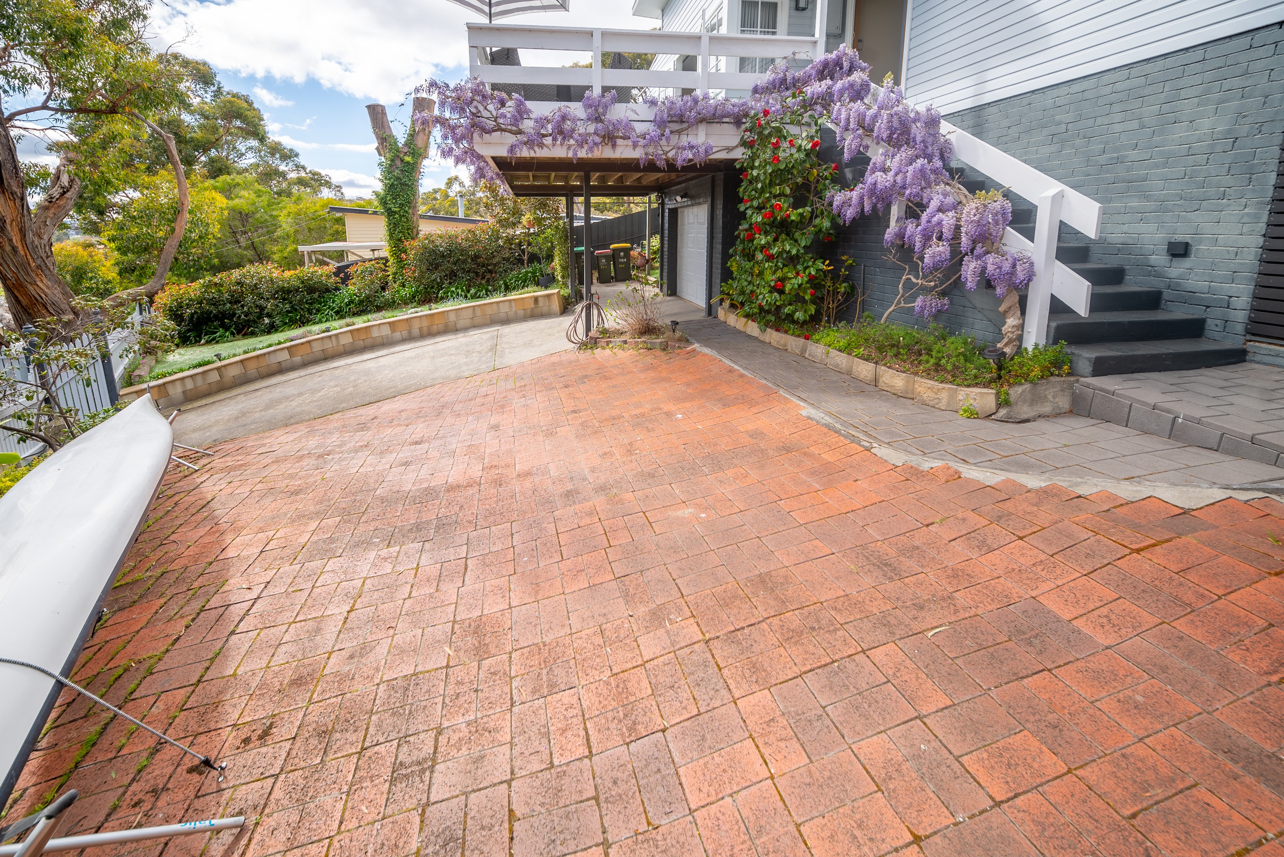 A brick-paved area beside the house, with wisteria over the deck and stairs up to the entry.