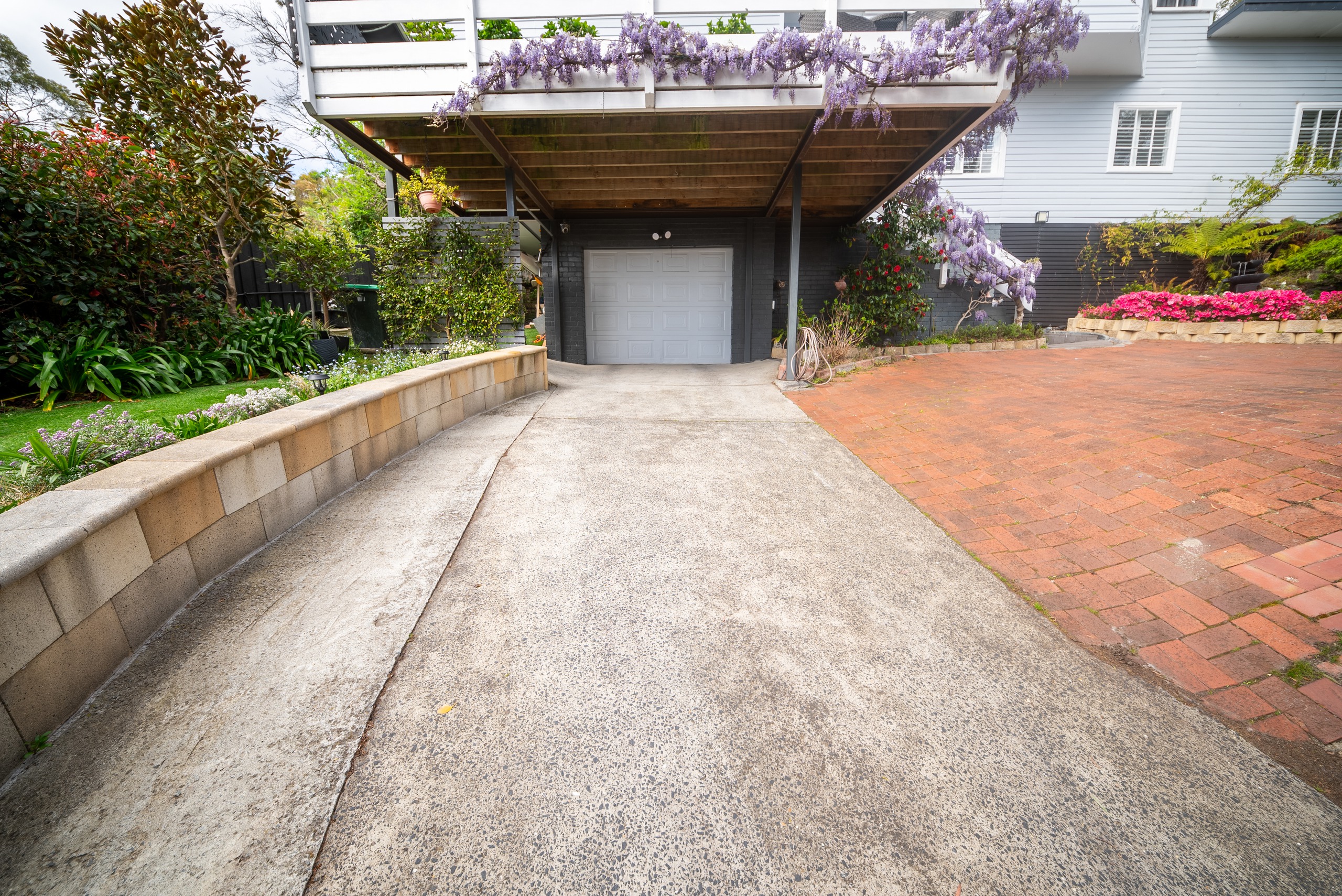 The driveway leading to the garage under the deck, edged by a sandstone retaining wall and garden beds.