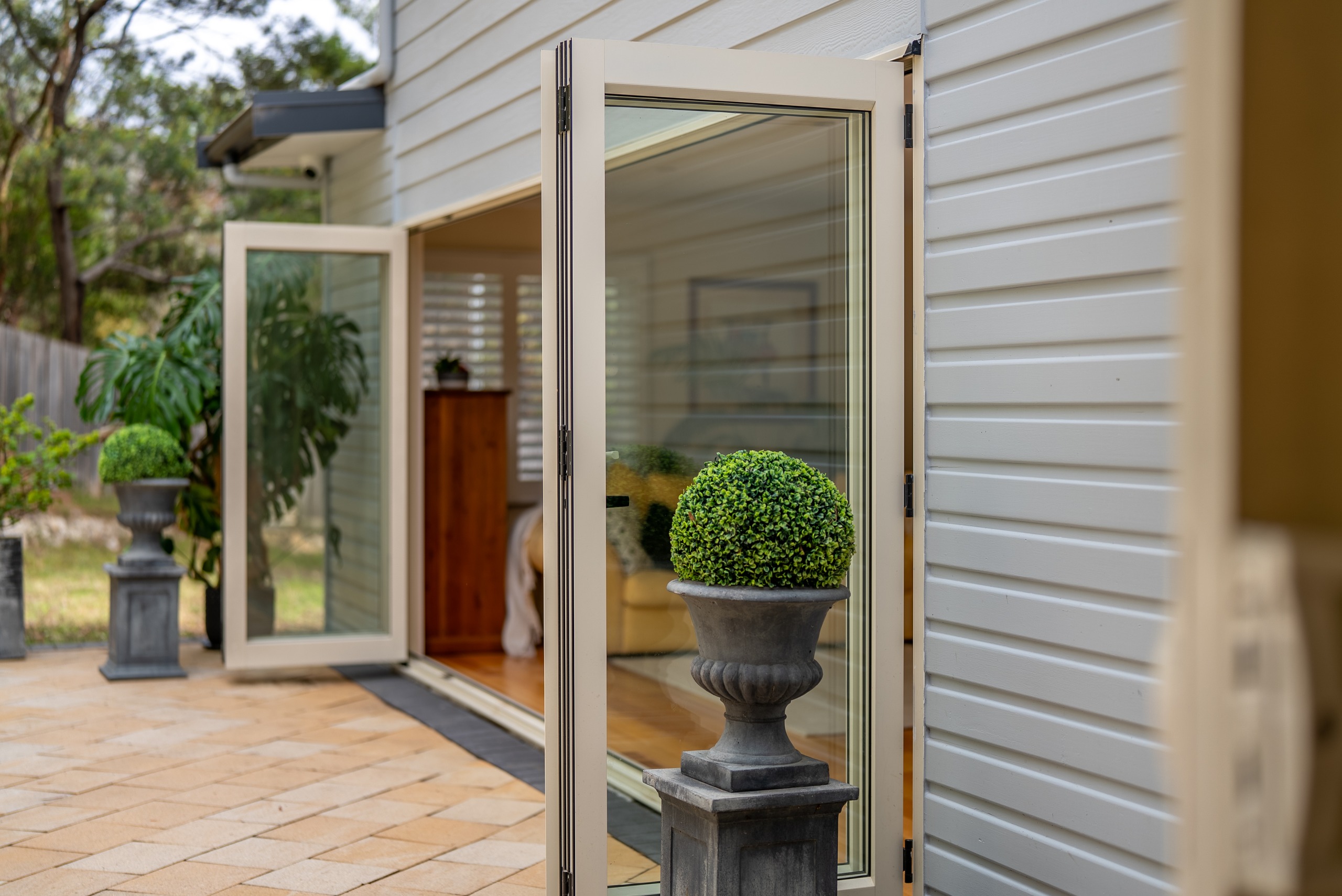 Bifold doors open from the house to the paved courtyard, with a topiary in a stone urn beside them.