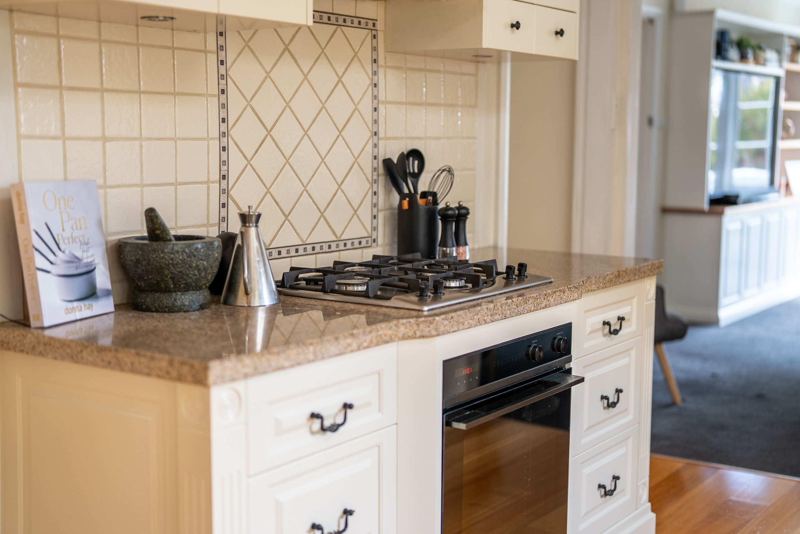 The kitchen cooktop and oven set into cream cabinetry with a tiled splashback.