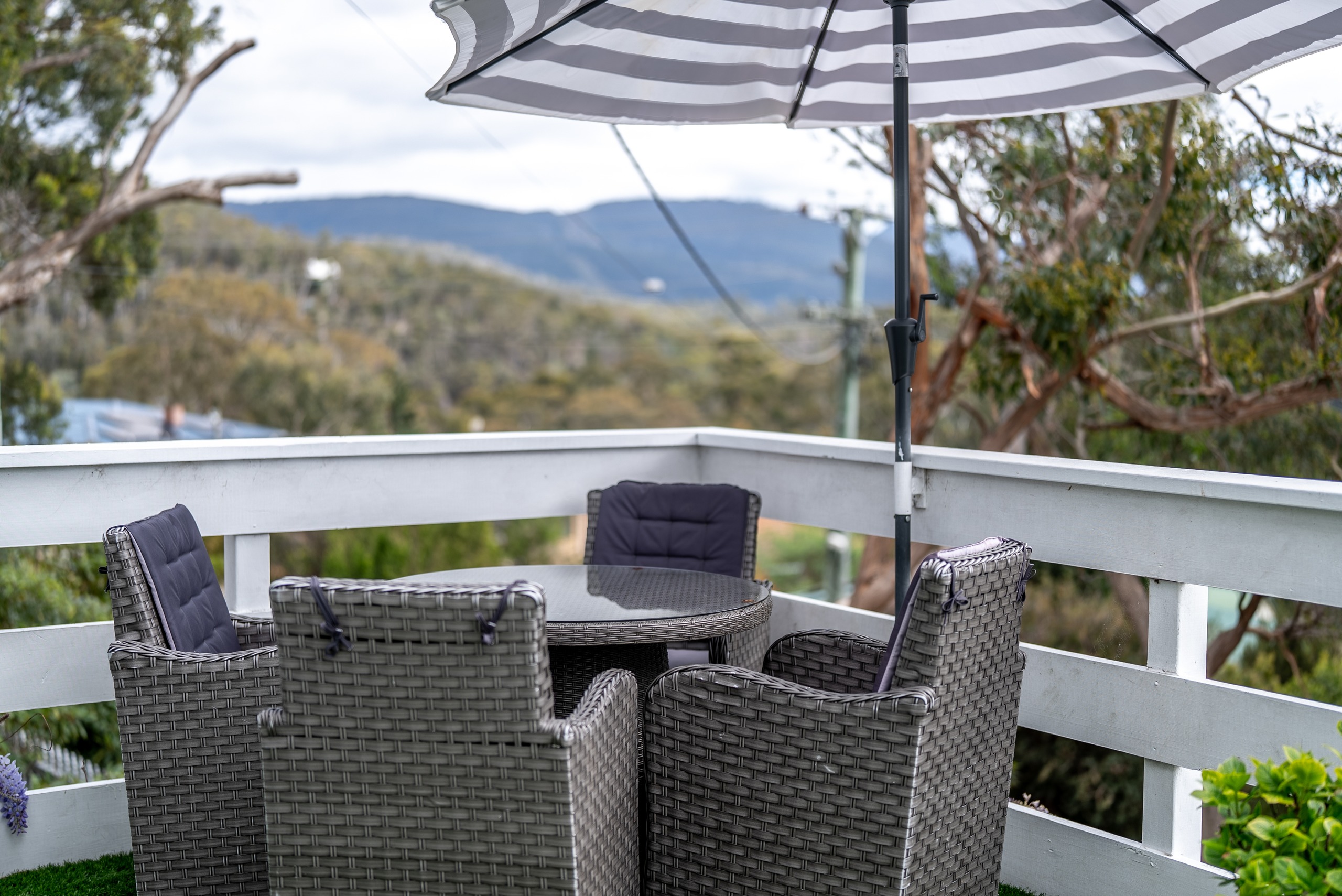 Wicker outdoor dining chairs and a table on the deck under an umbrella, looking out over the valley to the hills.