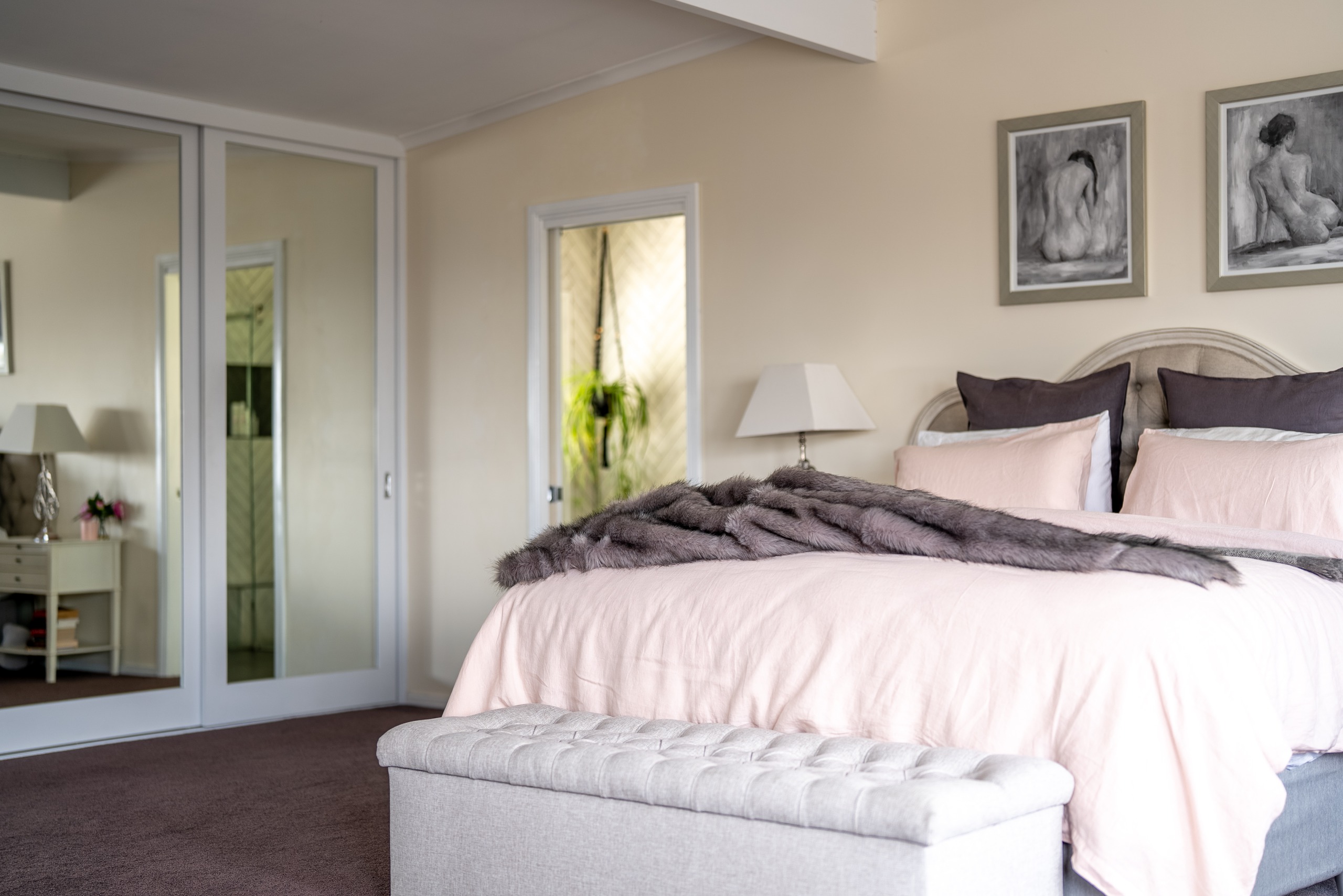 The main bedroom with a king bed, a tufted ottoman at its foot and mirrored wardrobe doors.