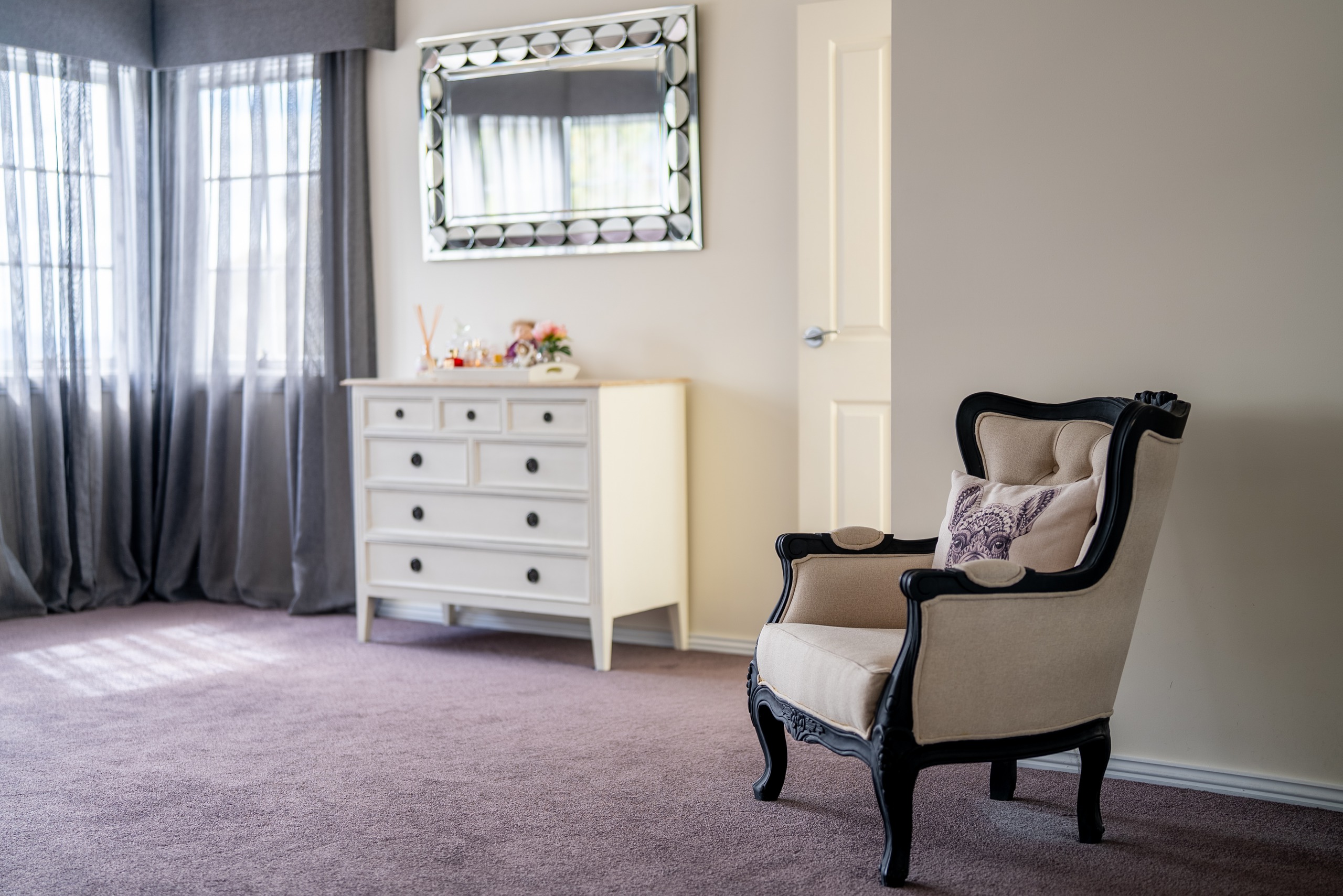 A corner of the main bedroom with a chest of drawers, a mirror and an upholstered armchair.