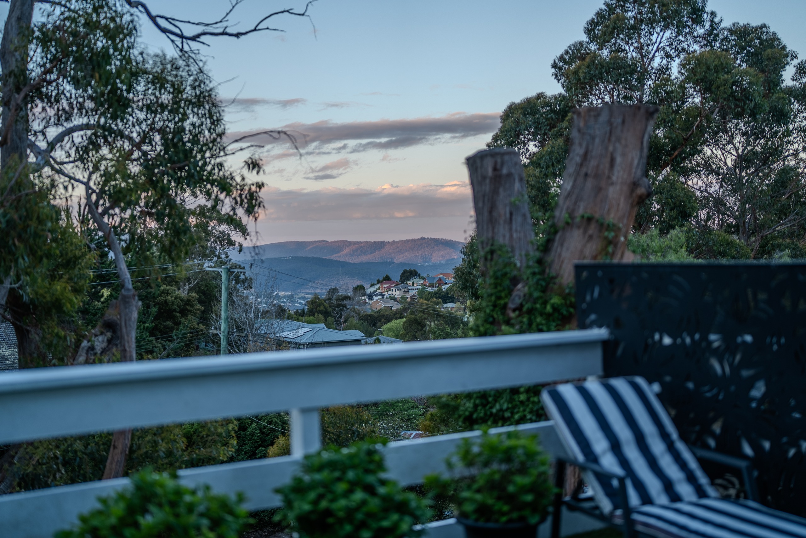 The deck at dusk with a striped lounger, looking out over the trees to the hills.