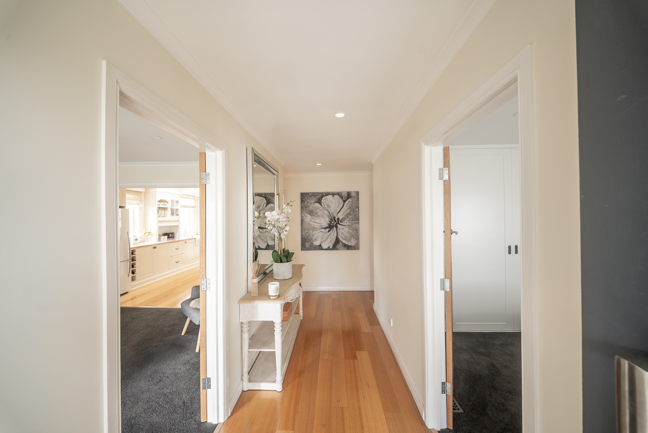 A hallway with timber floors and a console table, with doorways opening to the kitchen and to a bedroom.