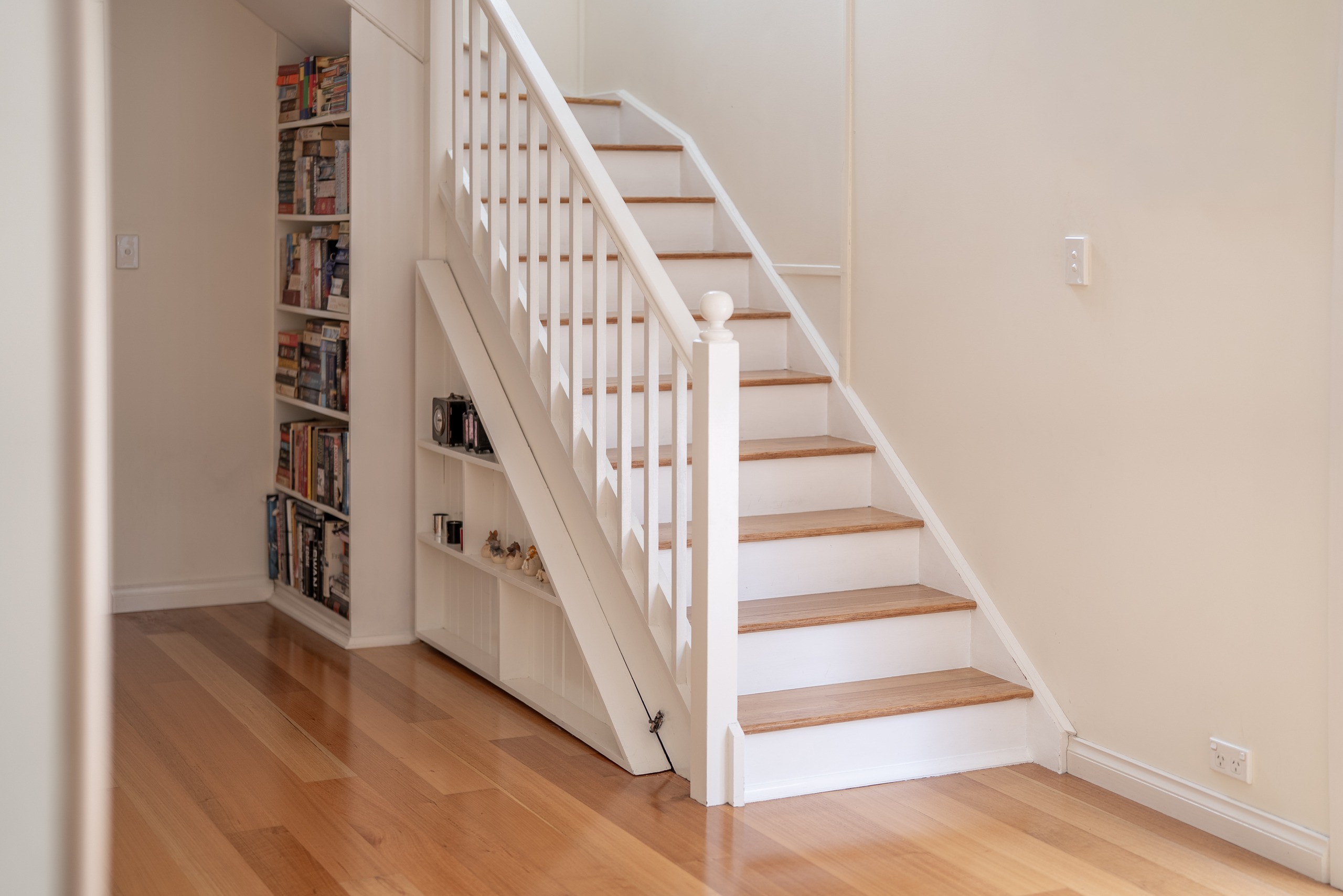 A white timber staircase with built-in bookshelves beneath and family photographs on the wall.
