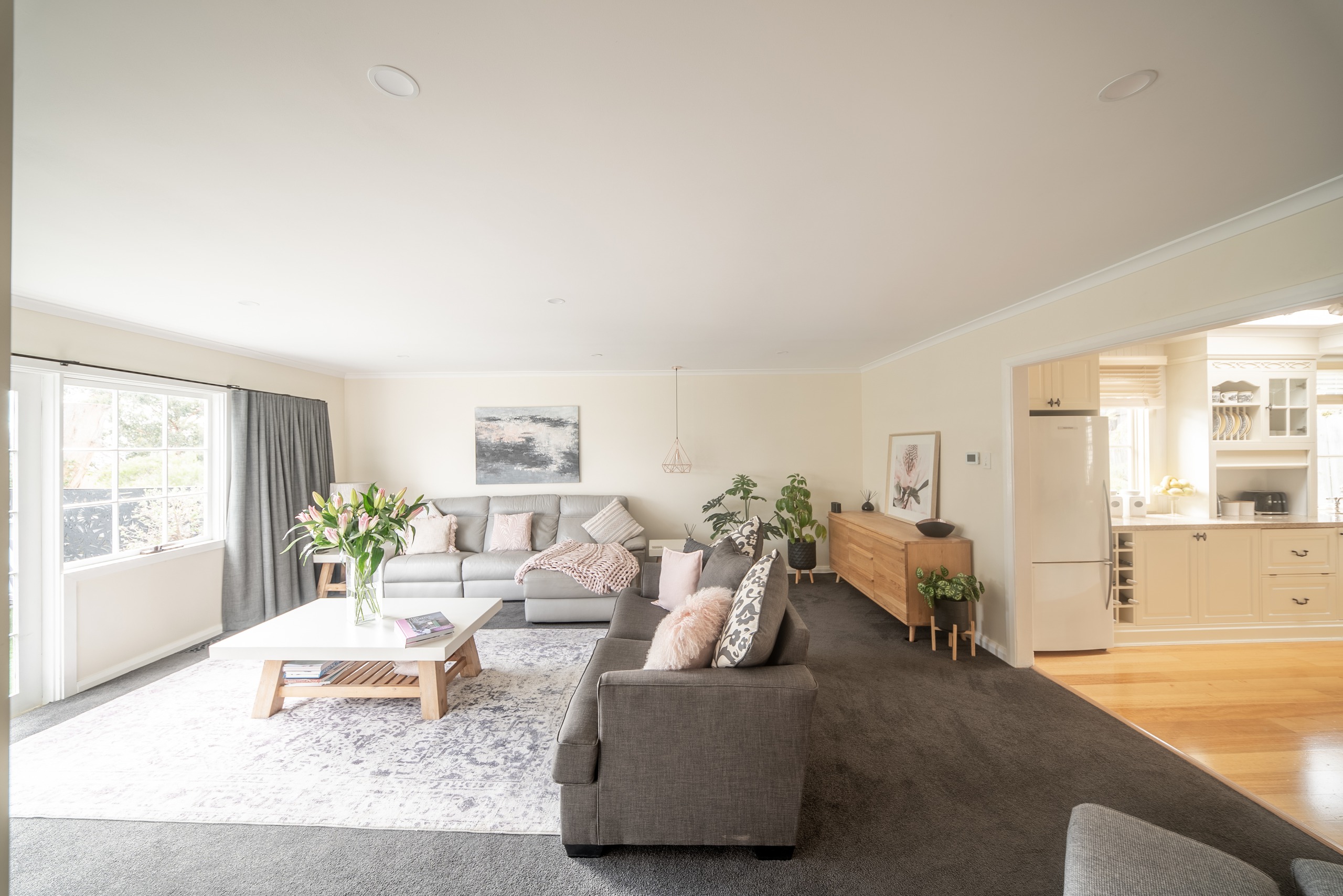 The living room with a grey sofa, a white coffee table on a patterned rug, and an opening through to the kitchen.