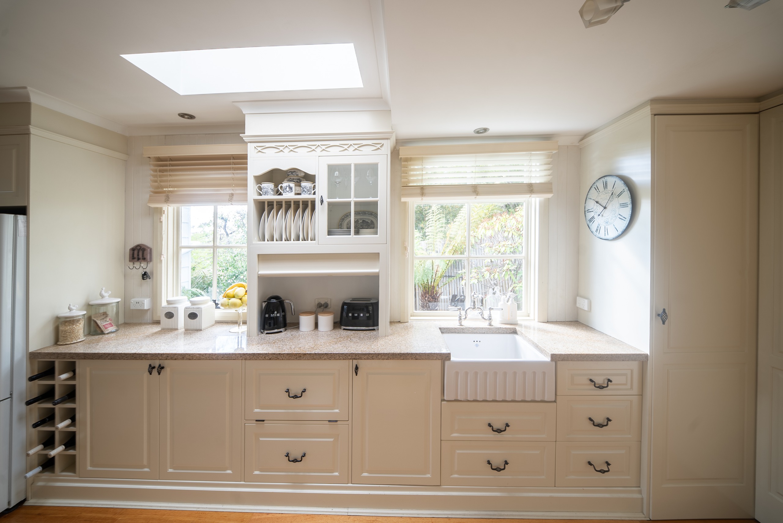 The classic kitchen with cream cabinetry, a butler sink under the window, a plate rack and a skylight.