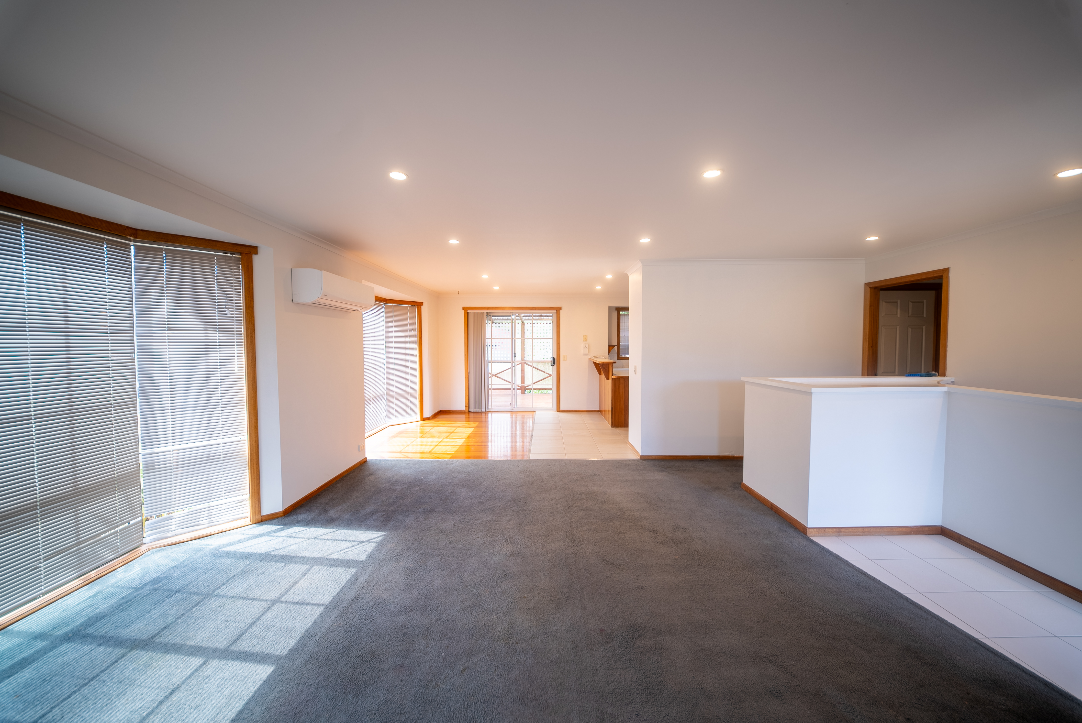Open plan lounge with grey carpet and a wall-mounted heat pump, with the dining area beyond.