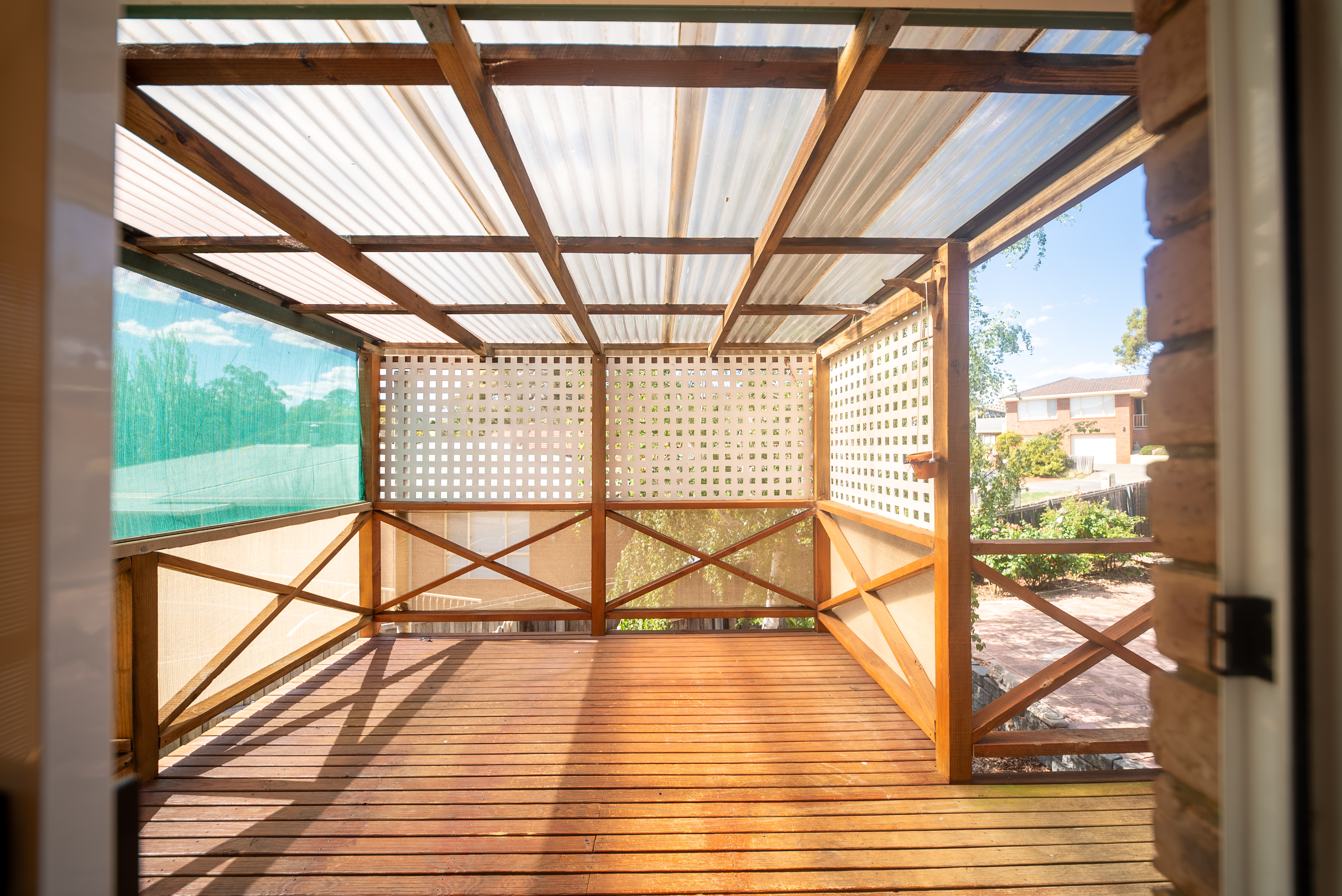 Covered deck off the dining area, with a timber floor, lattice screens and a translucent roof.