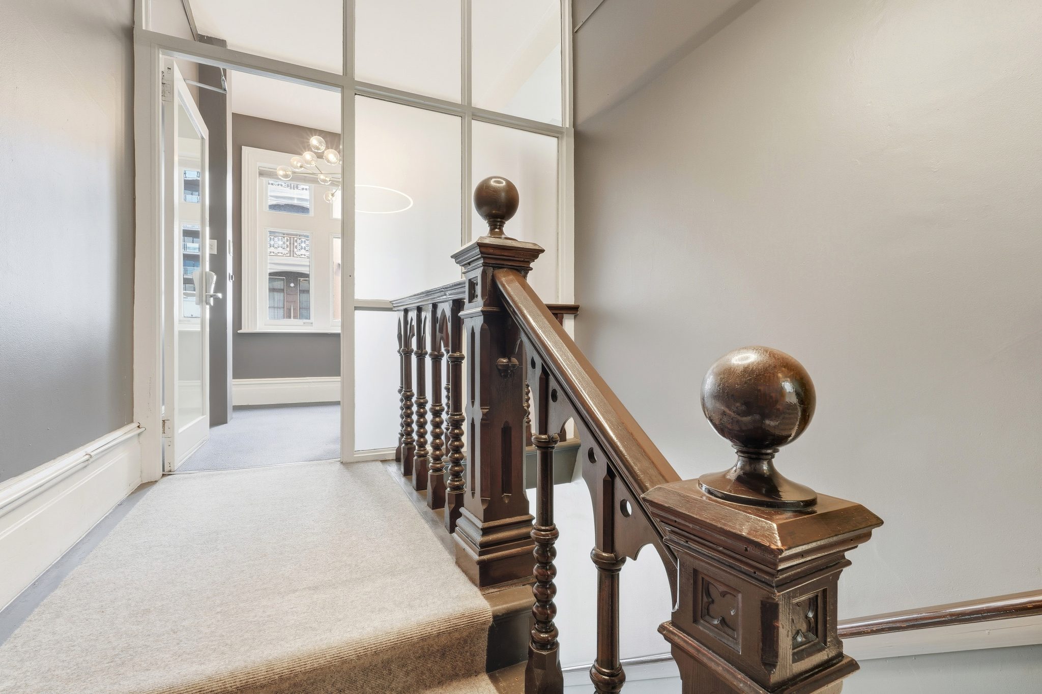 Carpeted landing at the top of a timber staircase with carved newel posts and a glazed partition.