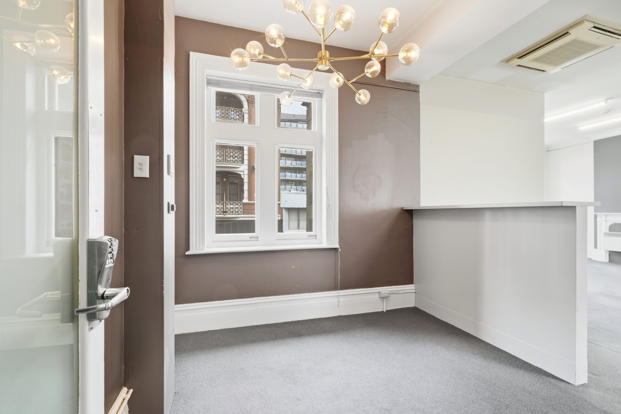 Reception area seen from the entry door, with a brown feature wall, sash window and globe pendant light.