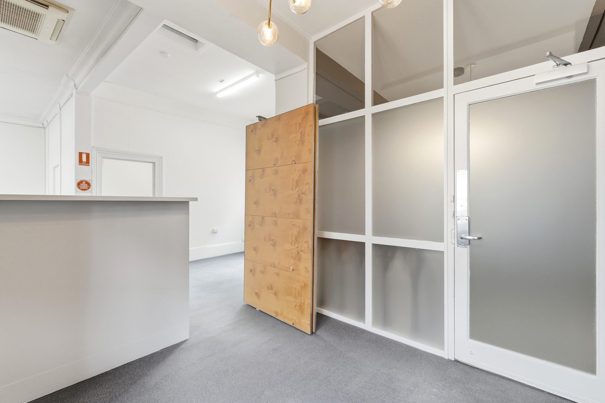 Reception counter beside a frosted glass entry door and partition, with a plywood sheet leaning against it.