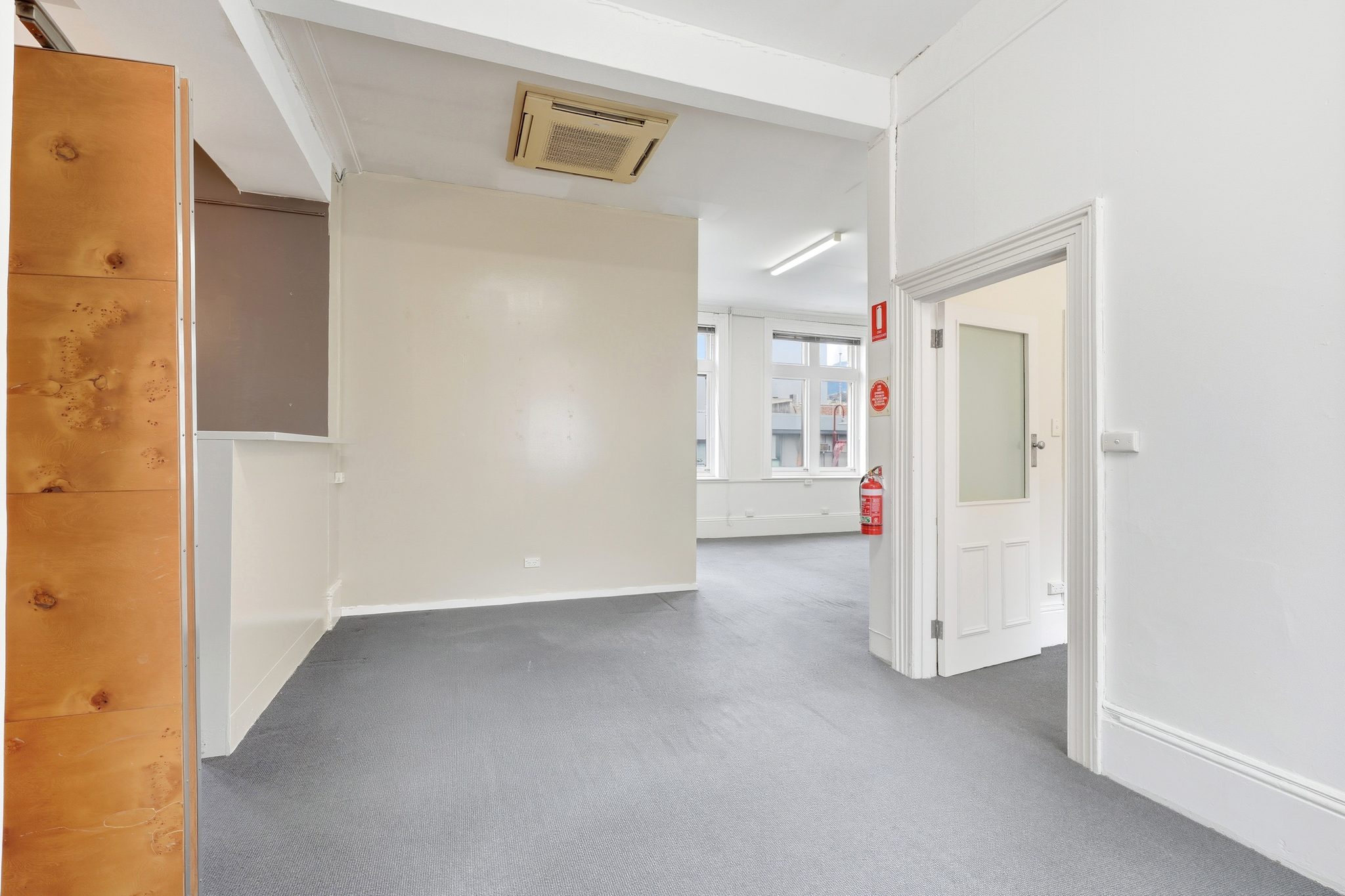 Carpeted floor with a dividing wall, a doorway through to an adjoining room and a fire extinguisher.