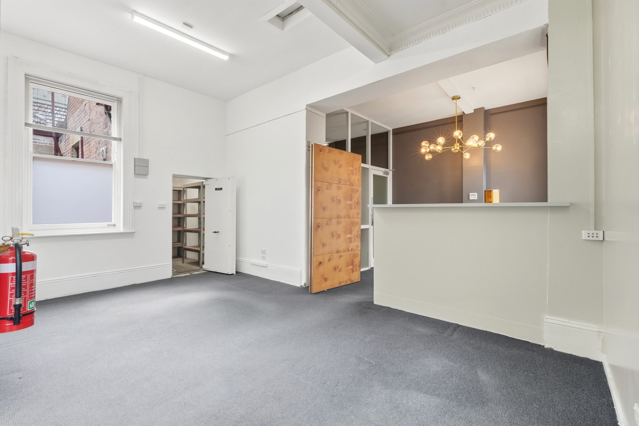 Room with an open strongroom door and shelving inside, and a counter with an opening to the next space.