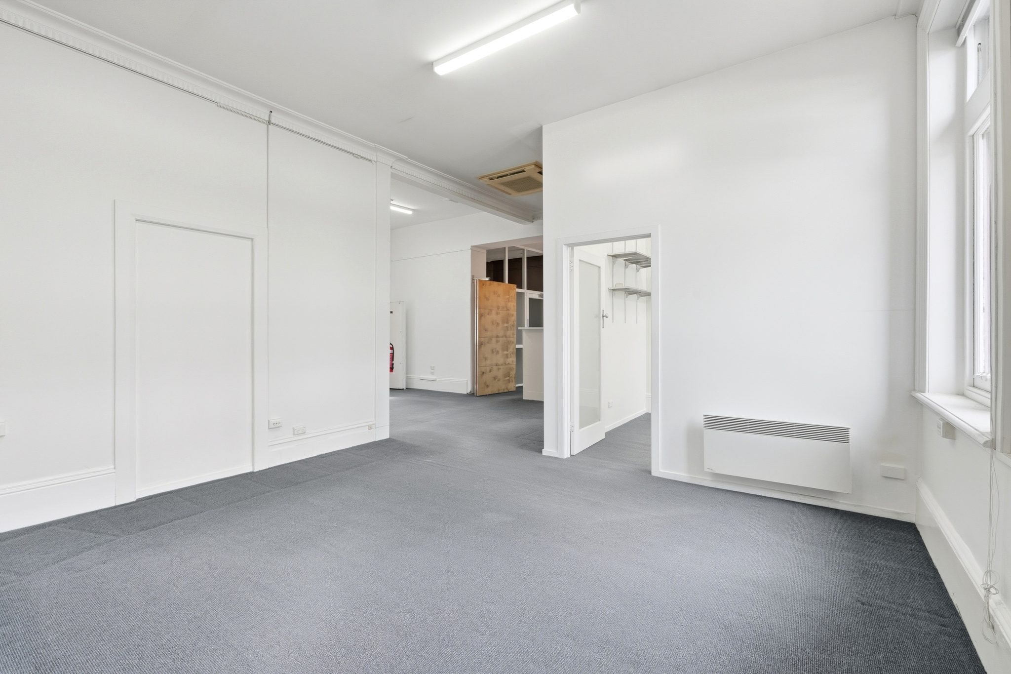 Open carpeted floor with a panel heater, a doorway to a store with shelving and a window to one side.