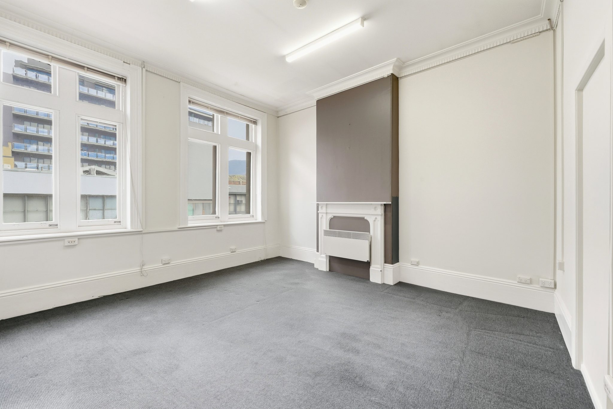 Carpeted room with two sash windows and a painted mantelpiece with a heater set into the opening.