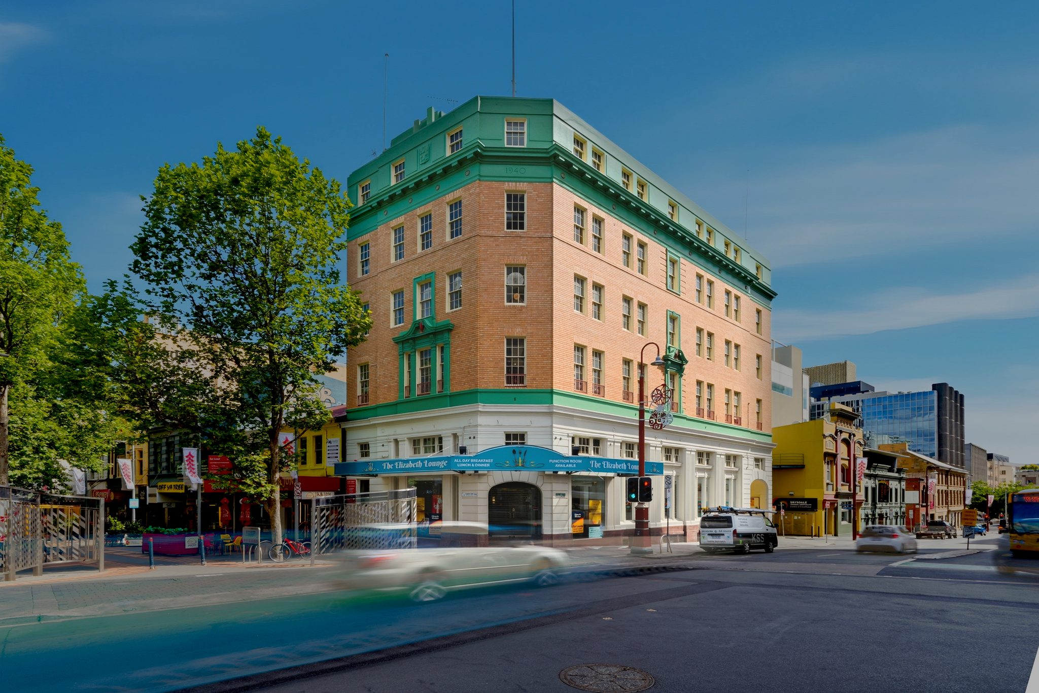 Corner brick building on Elizabeth Street with ground floor shopfronts and passing traffic.