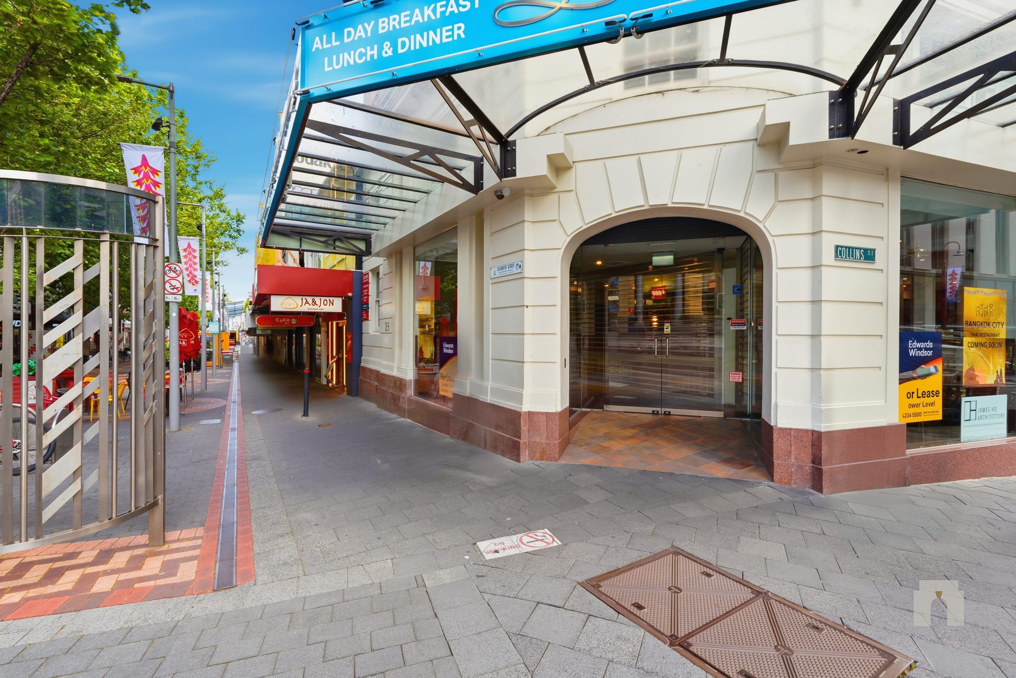 Arched corner entry with glass doors at the Elizabeth and Collins Street corner, paved footpath.