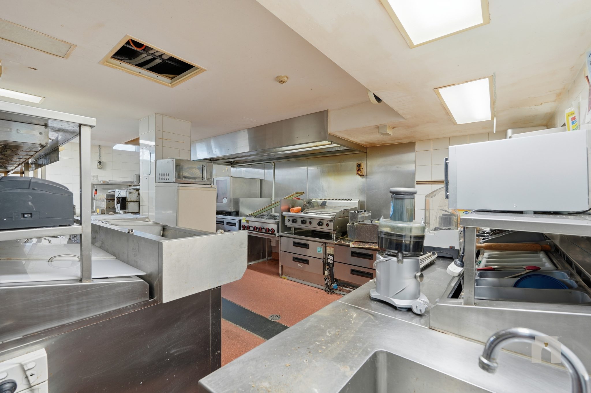 Commercial kitchen with stainless steel benches, cooktop and grill under an extraction canopy.