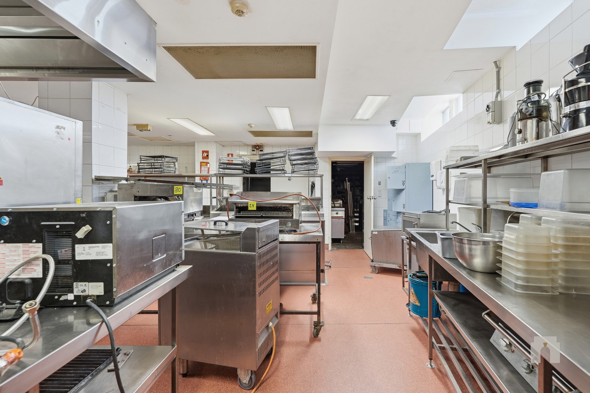Commercial kitchen looking towards a rear doorway, stainless benches and mobile equipment.