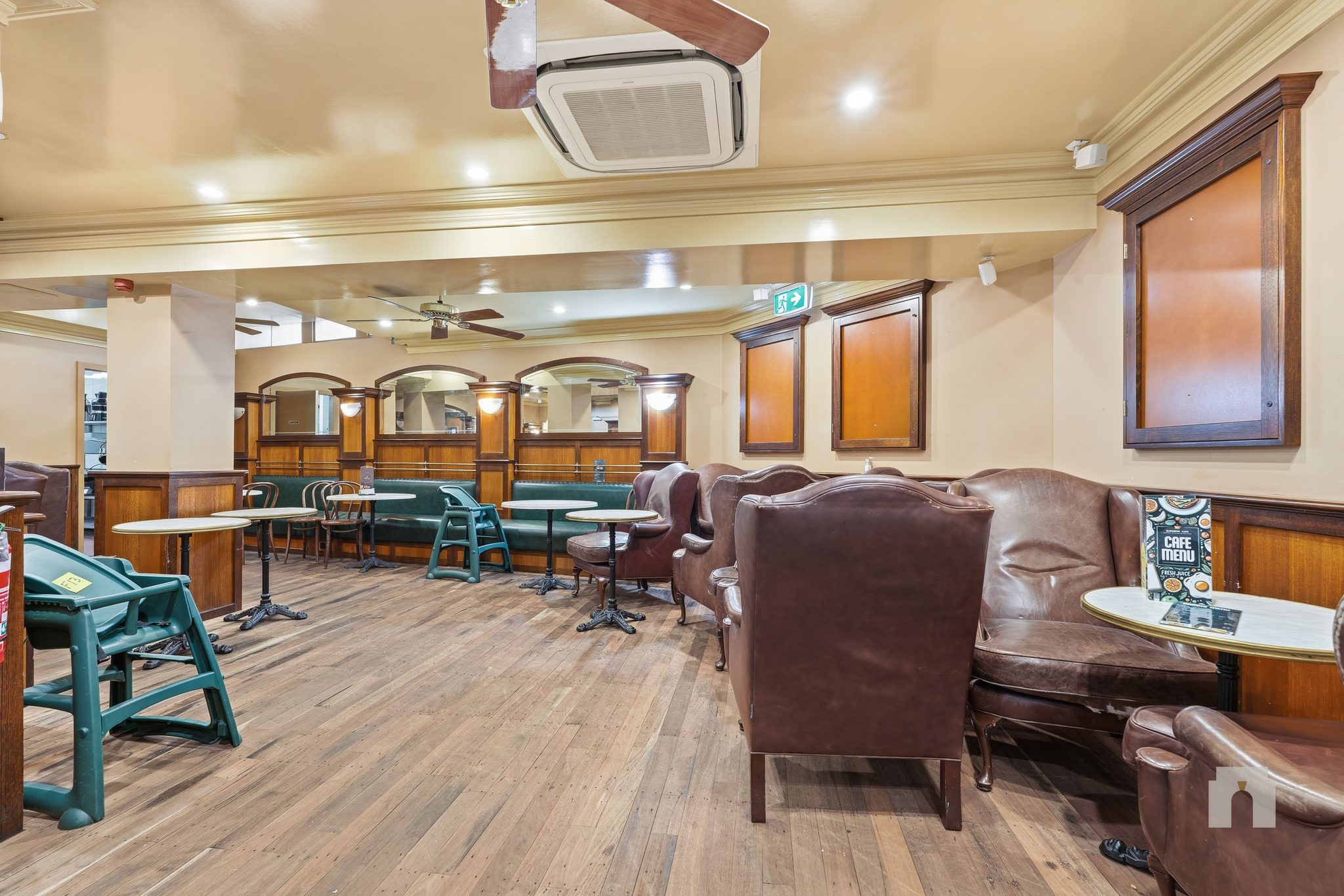 Dining area with leather armchairs, cafe tables and green banquettes along panelled walls.