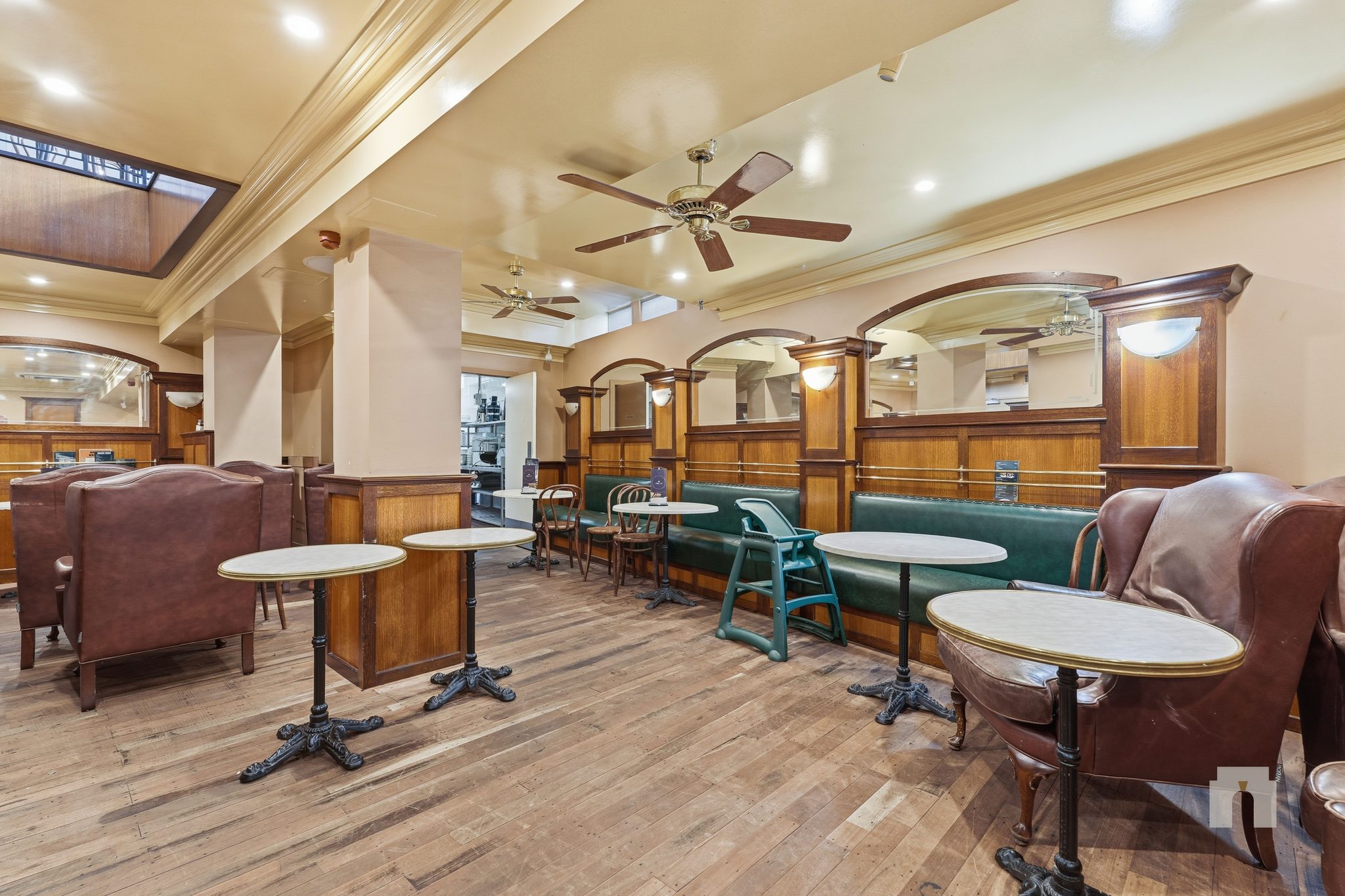 Dining room with green banquette seating under arched mirrors and marble topped cafe tables.