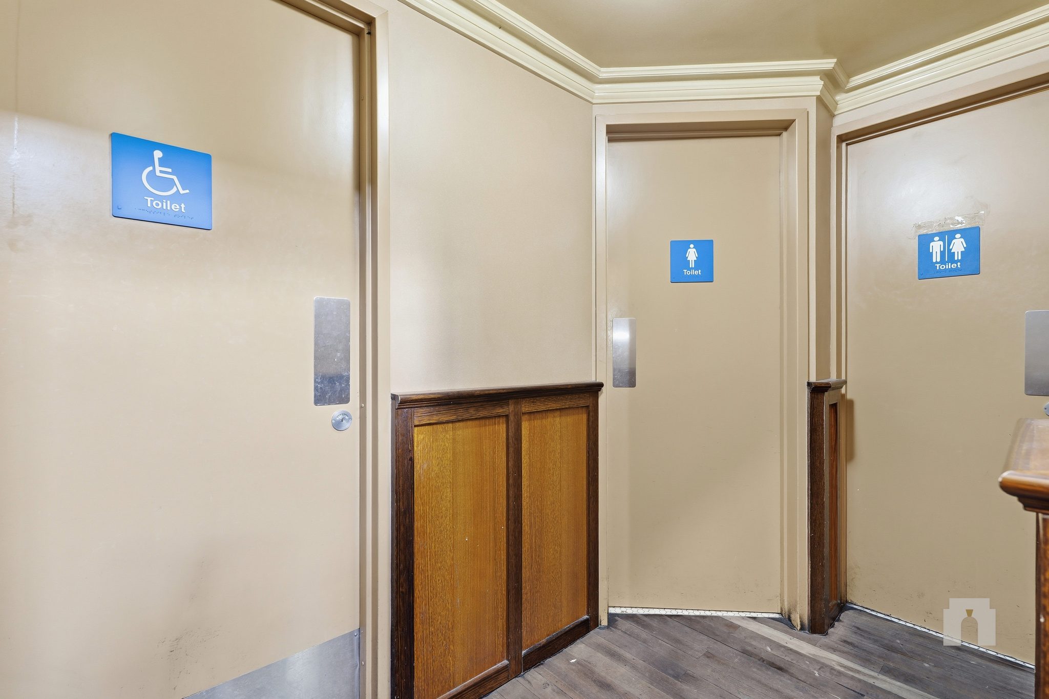 Toilet lobby with accessible and gendered toilet doors above timber dado panelling.