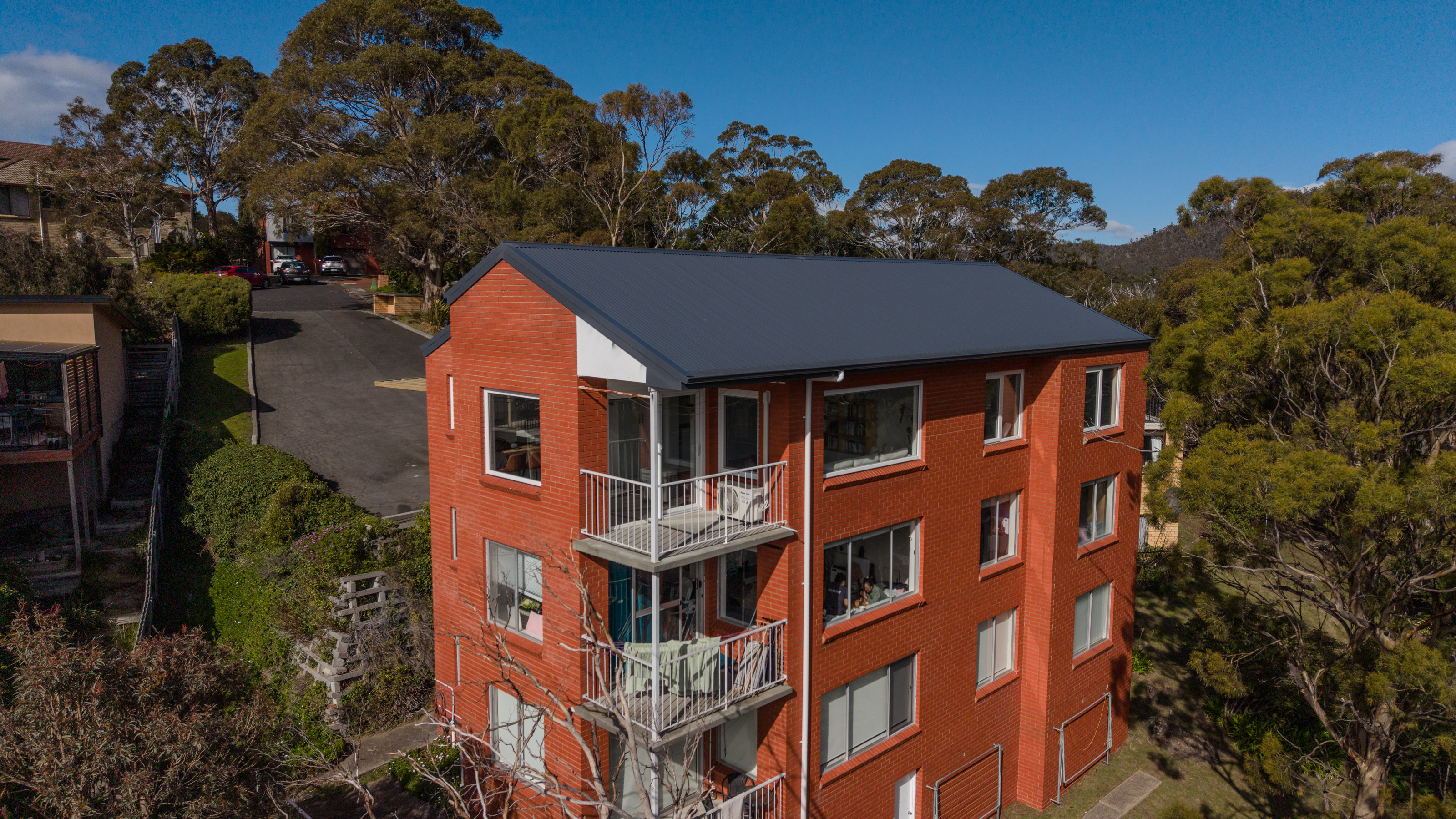 Aerial view of the red brick apartment block from above the driveway, with a new dark Colorbond roof and stacked balconies.