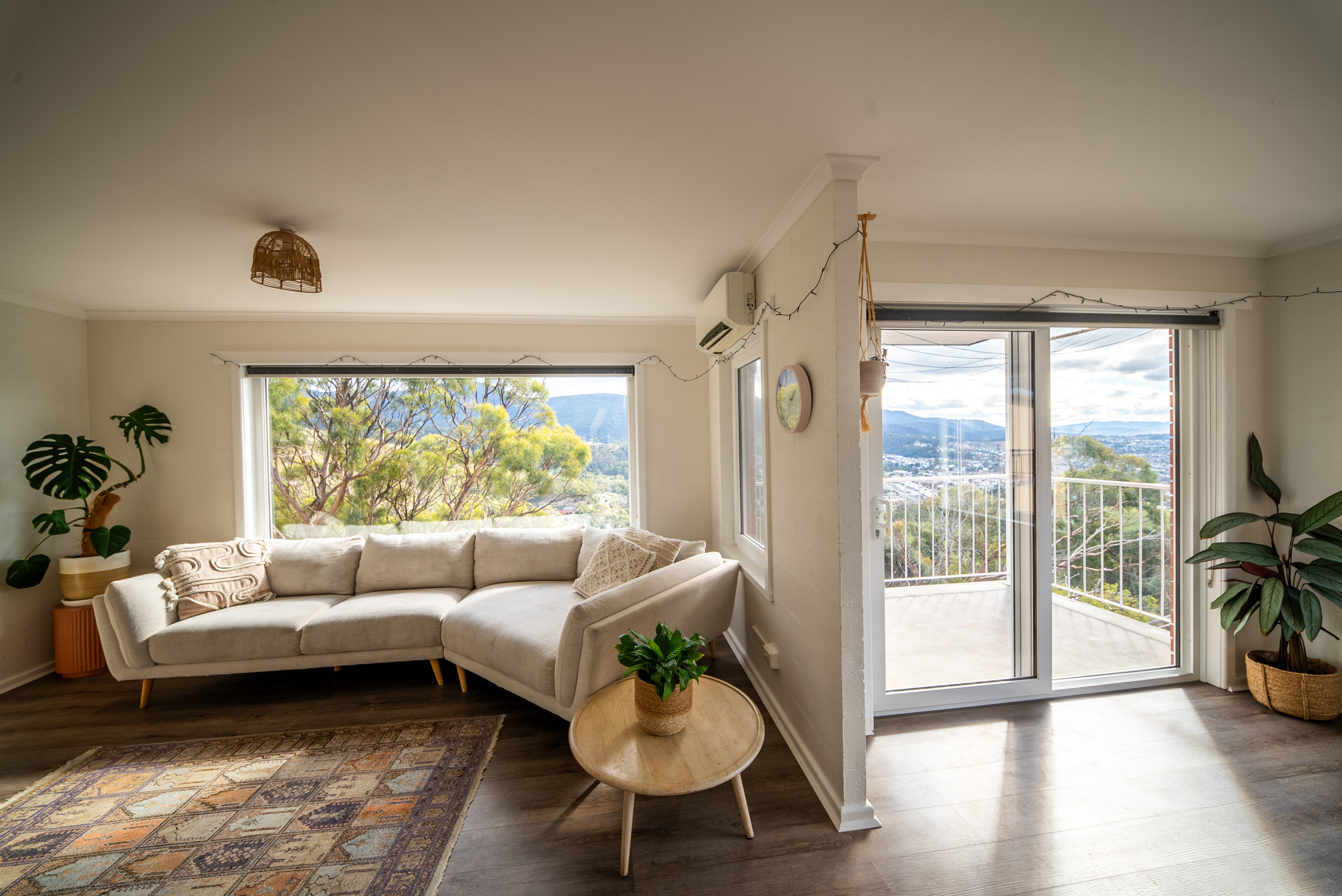 Living room with a pale sectional sofa under a picture window, a rug on timber look flooring, and a sliding door to the balcony.