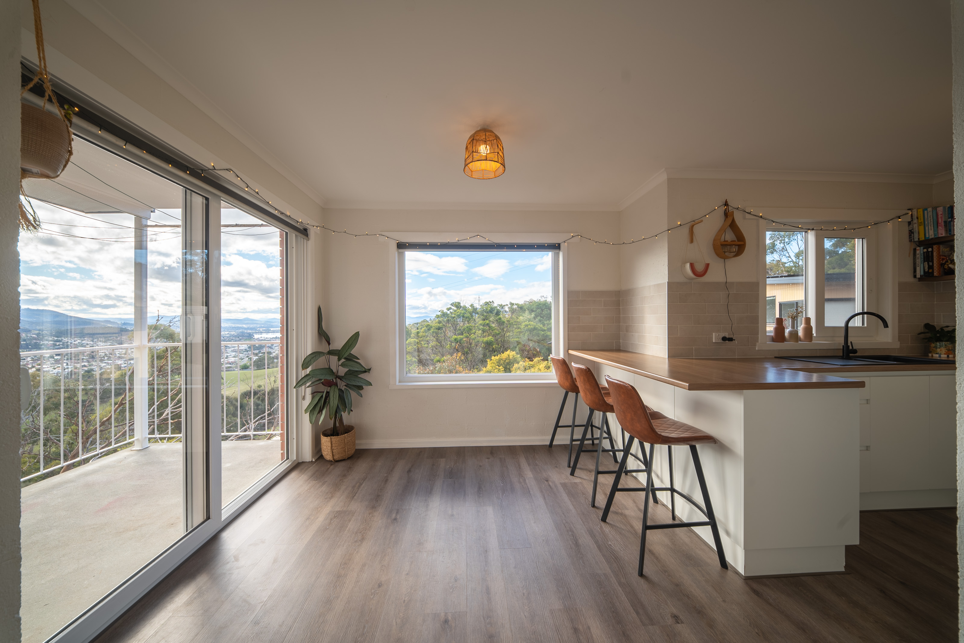Dining end of the living room, with three tan stools at the breakfast bar and a sliding door to the balcony.