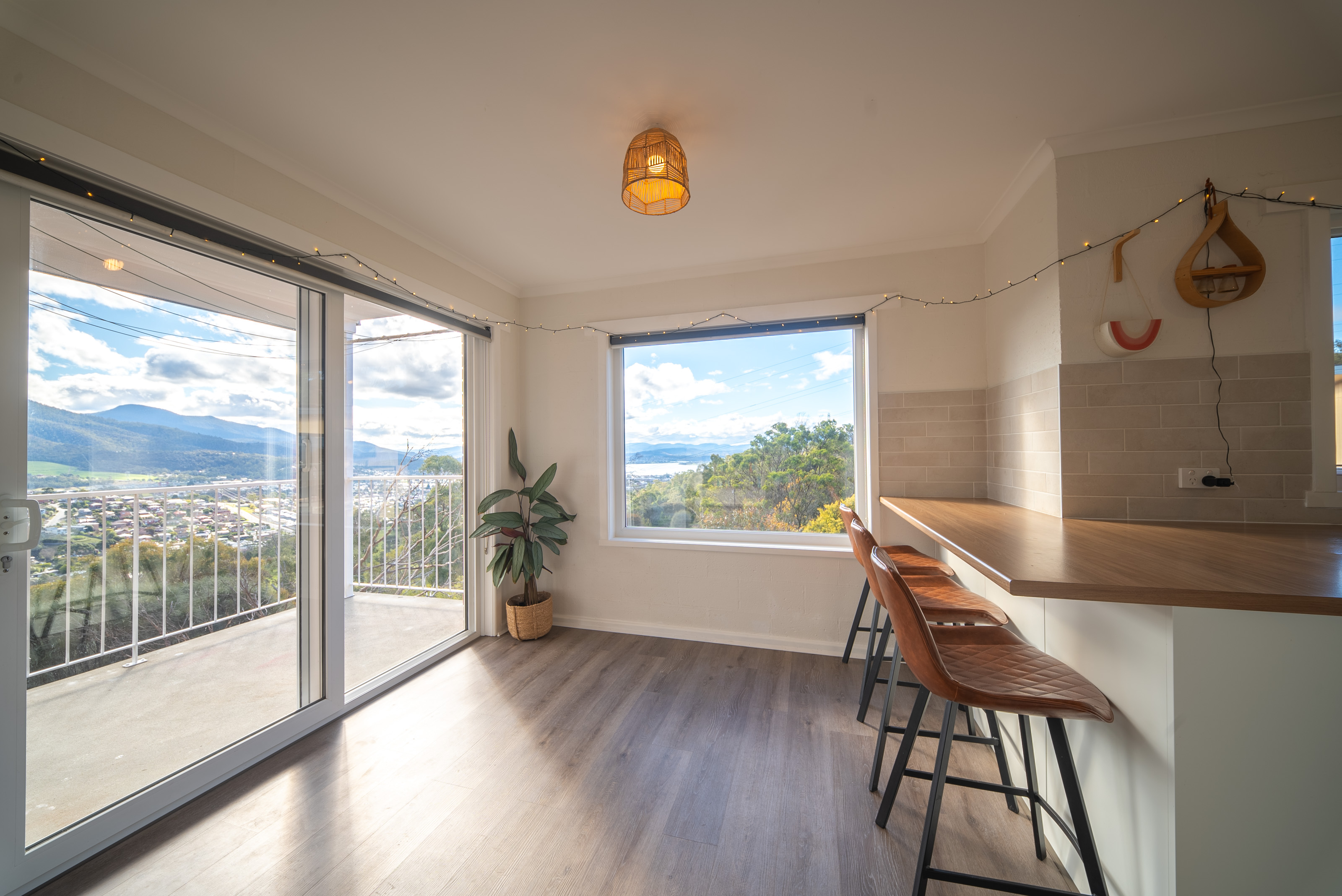 Dining area with the balcony door open to the view, the breakfast bar and tiled splashback to one side.