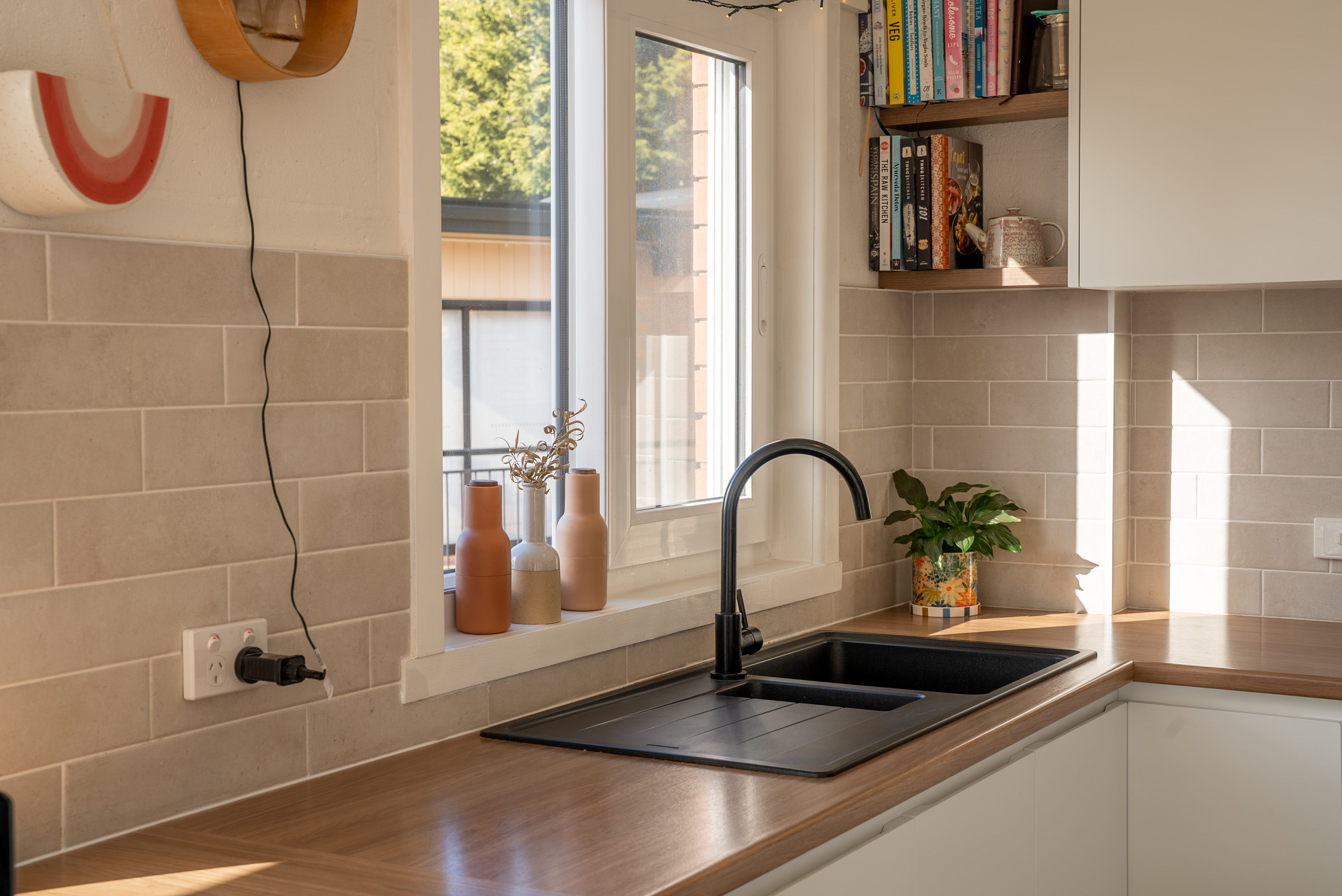 Kitchen bench with a black sink and tap set into the benchtop, below a window to the trees.