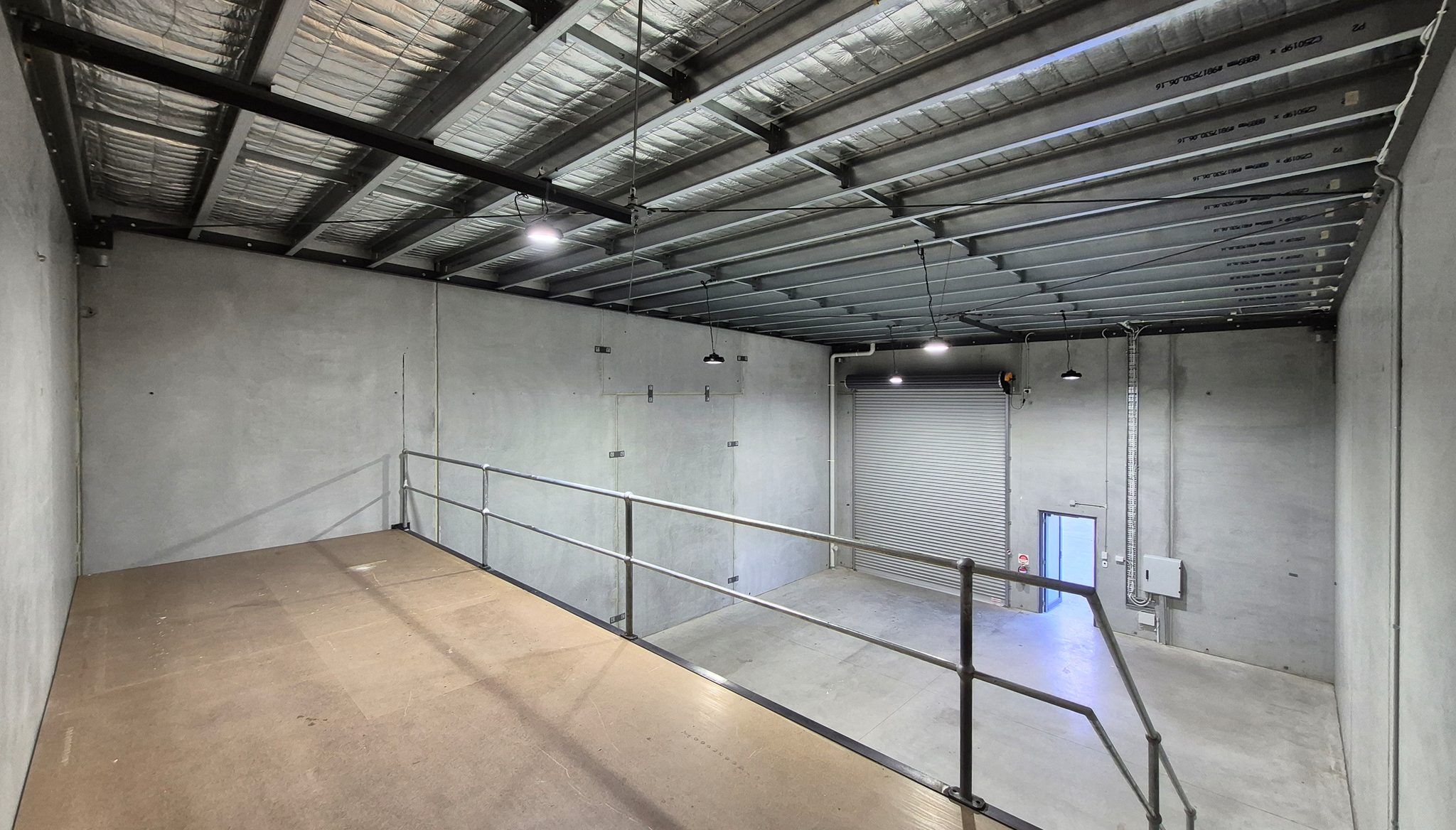 Mezzanine level with a steel guardrail, looking down over the floor towards the roller shutter door.
