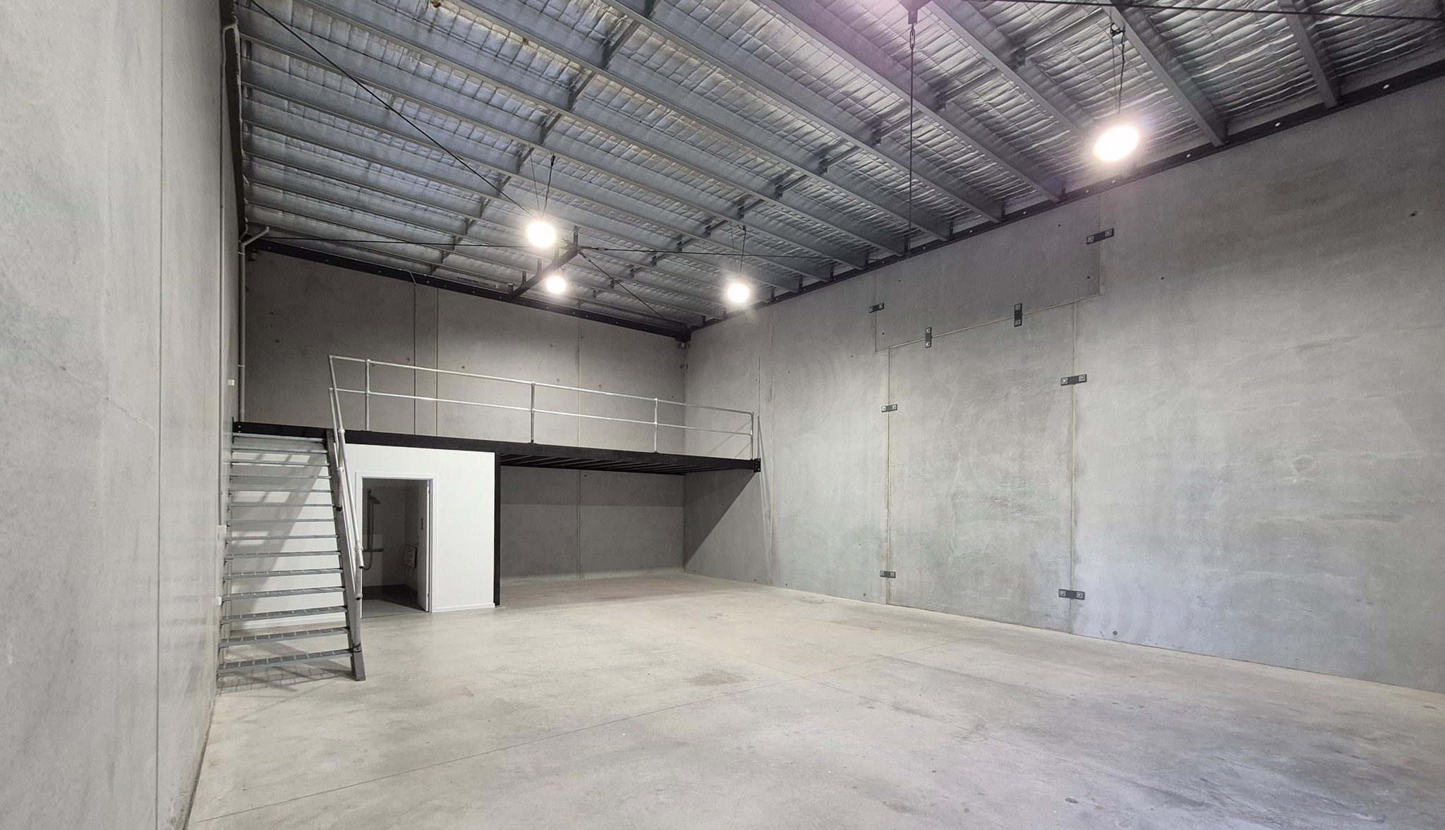 Warehouse interior from the opposite corner, mezzanine above an enclosed room, with stair access.