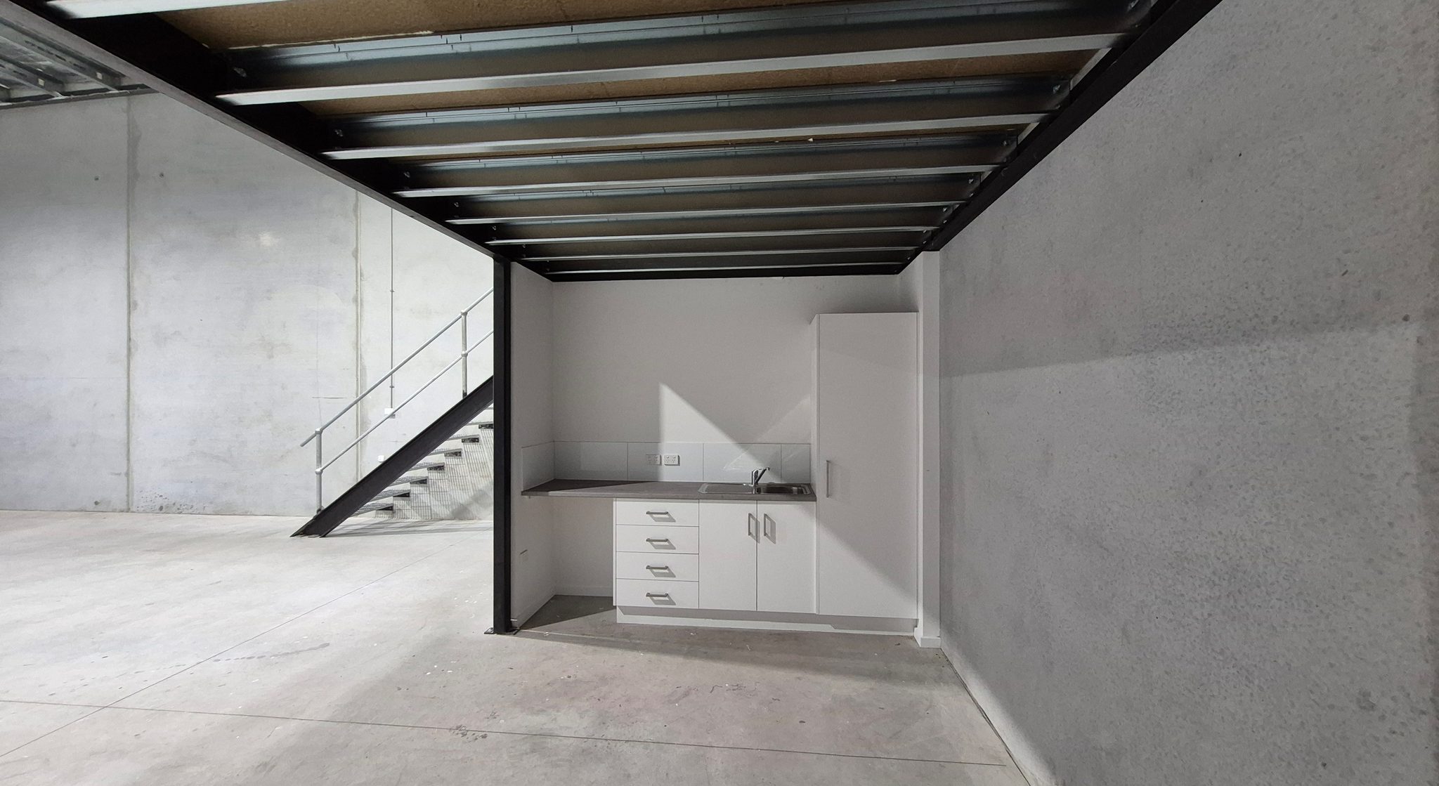 Kitchenette with sink and cabinets set beneath the mezzanine, stair alongside on the warehouse floor.