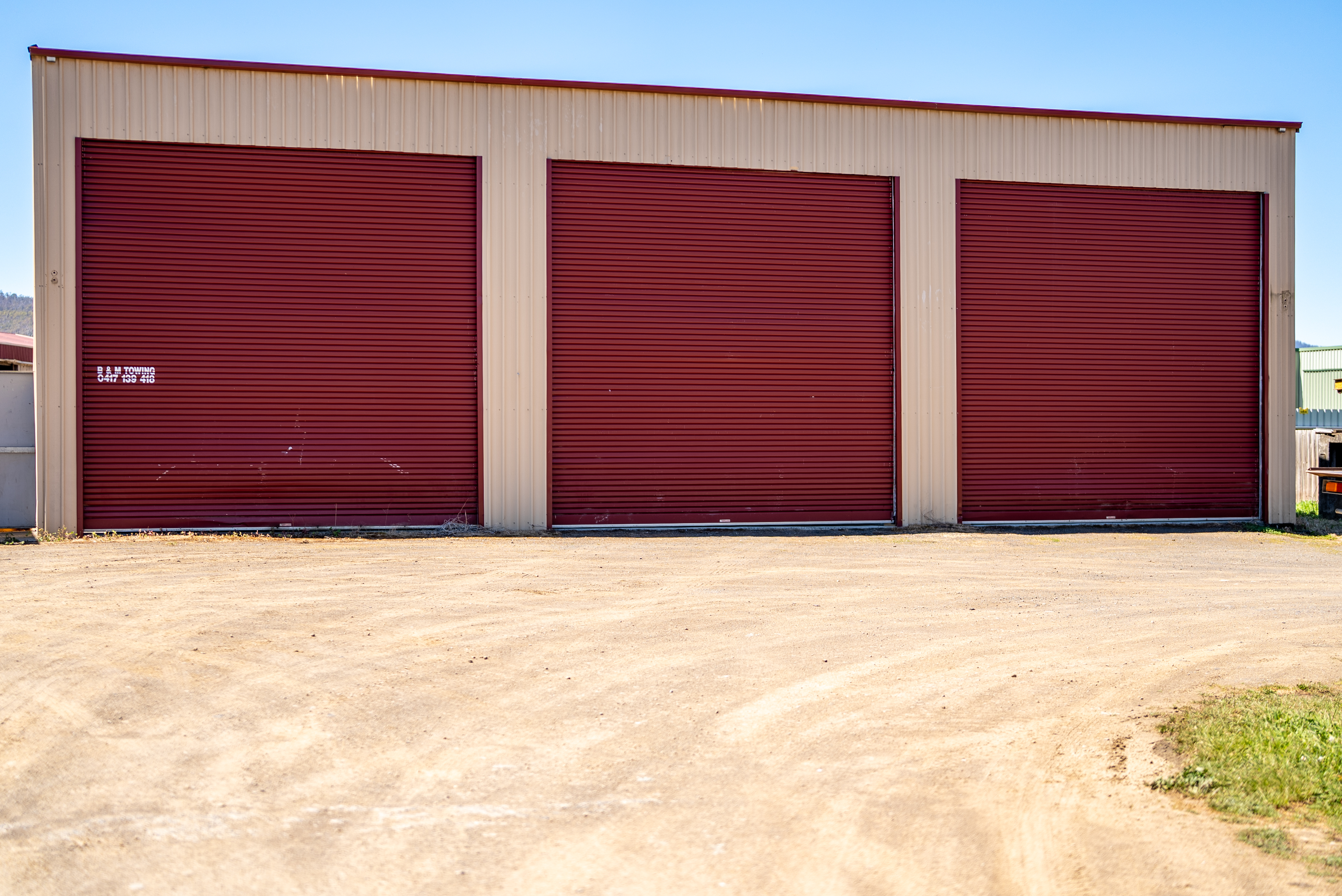 Front of the warehouse with three large red roller doors opening onto a wide gravel hardstand.