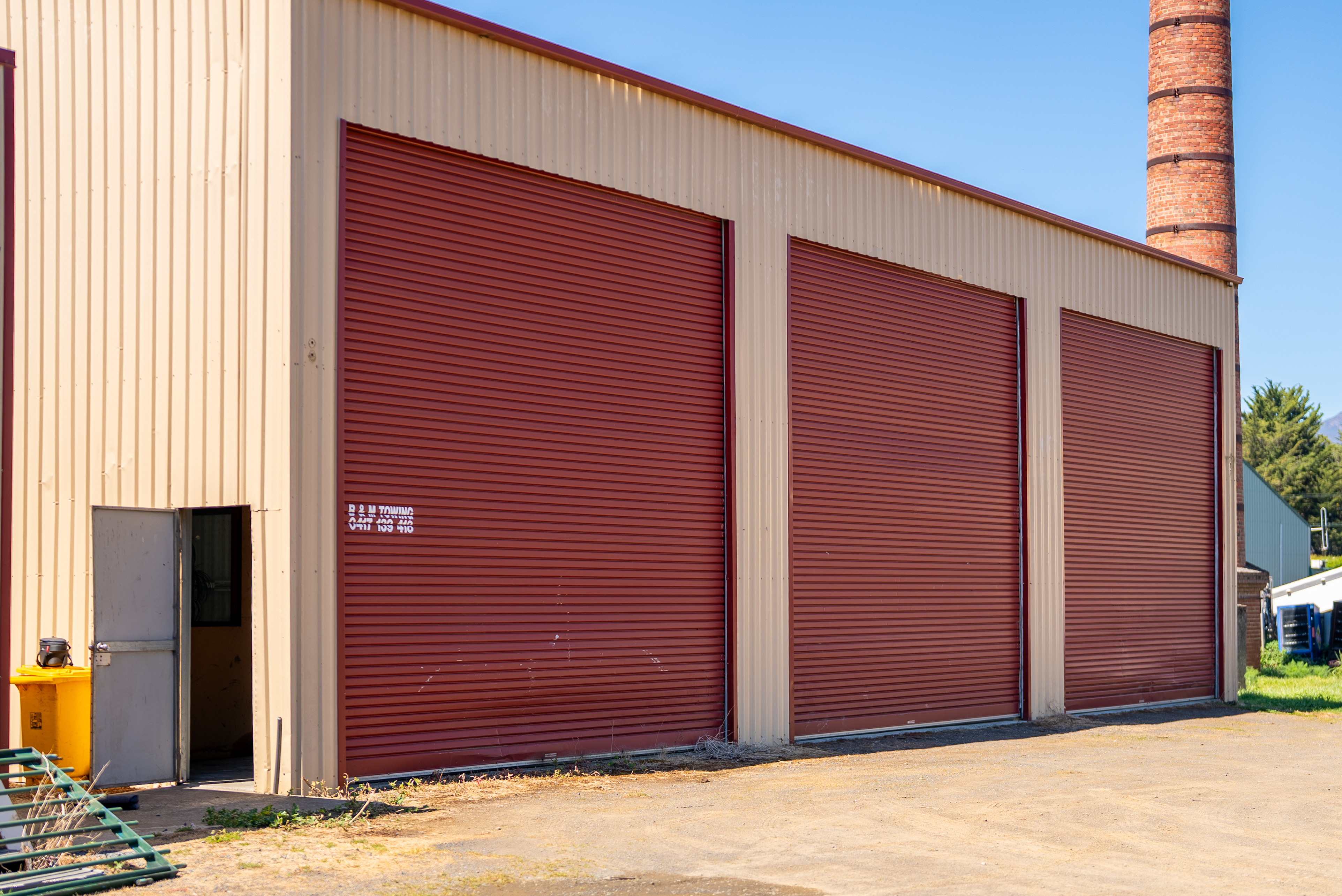 Side view of the roller doors and the personal access door, with a brick chimney beyond.
