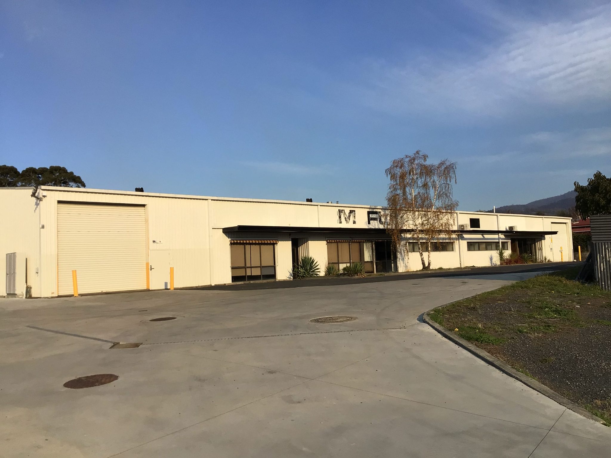 Long clad warehouse building with a roller shutter door and concrete hardstand across the front.
