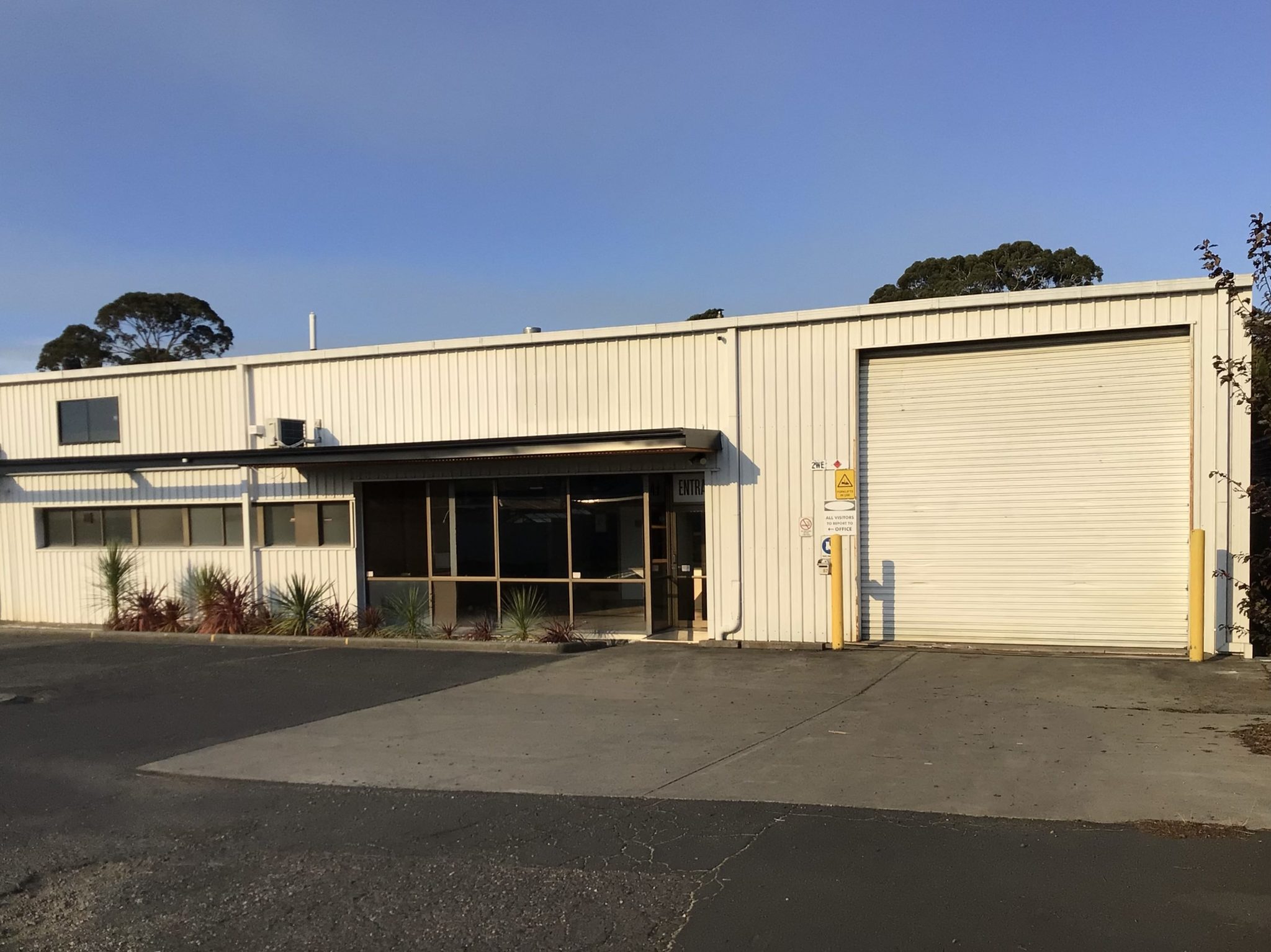 Glazed office entrance beside a roller shutter door, with visitor signage and a concrete apron.
