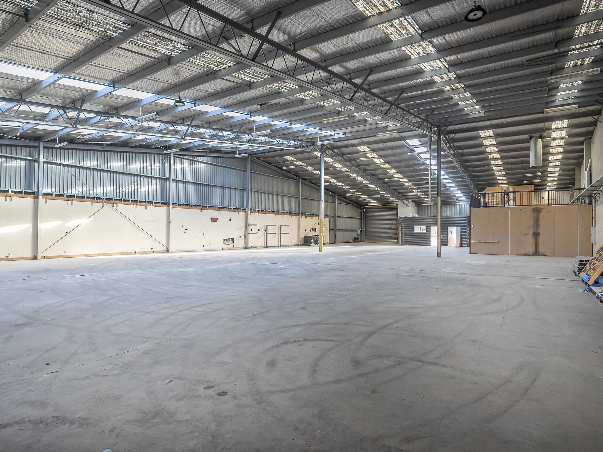 Empty warehouse floor with a concrete slab, steel portal frames and rows of roof skylights.